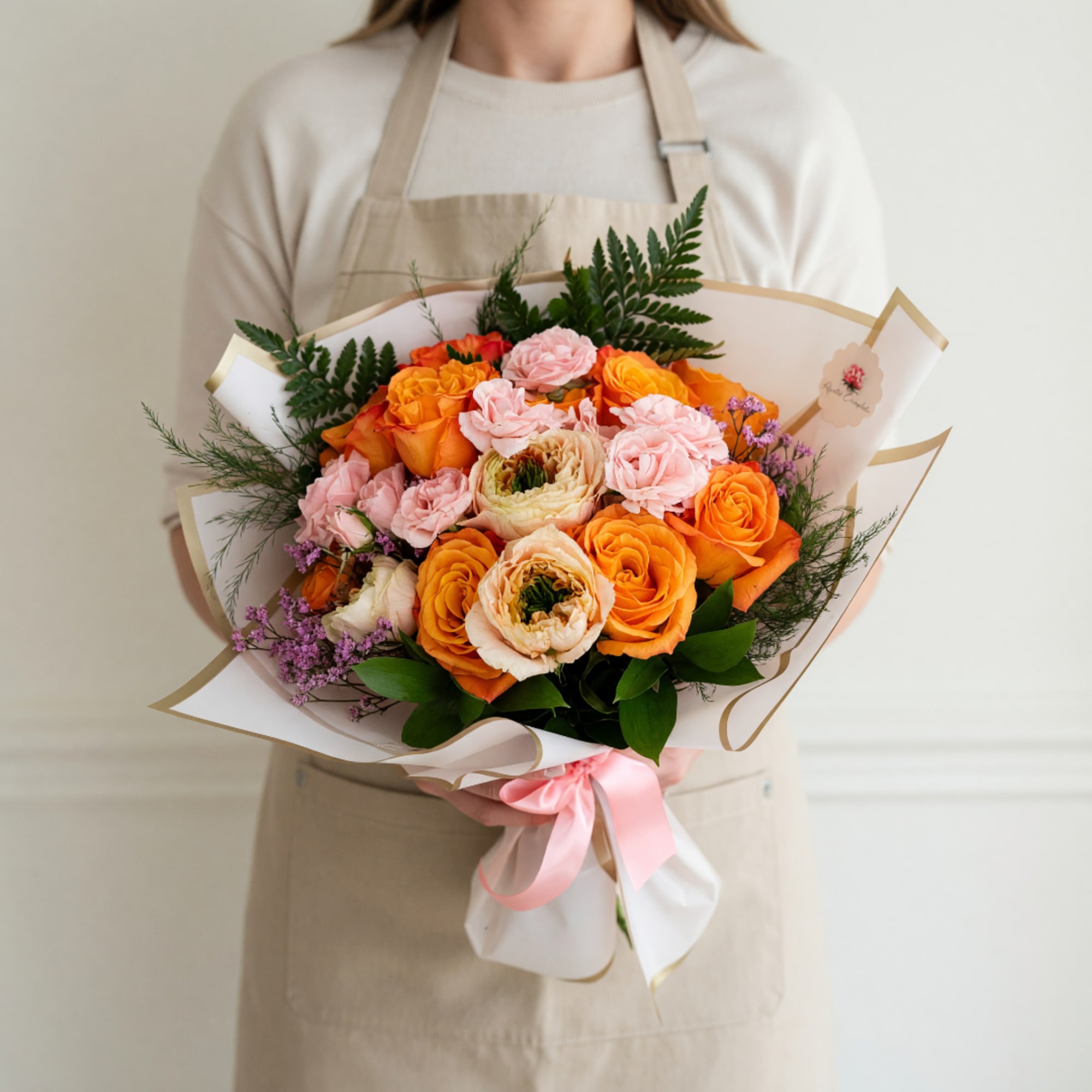 Bouquet of orange and pink roses wrapped in white paper with a pink ribbon