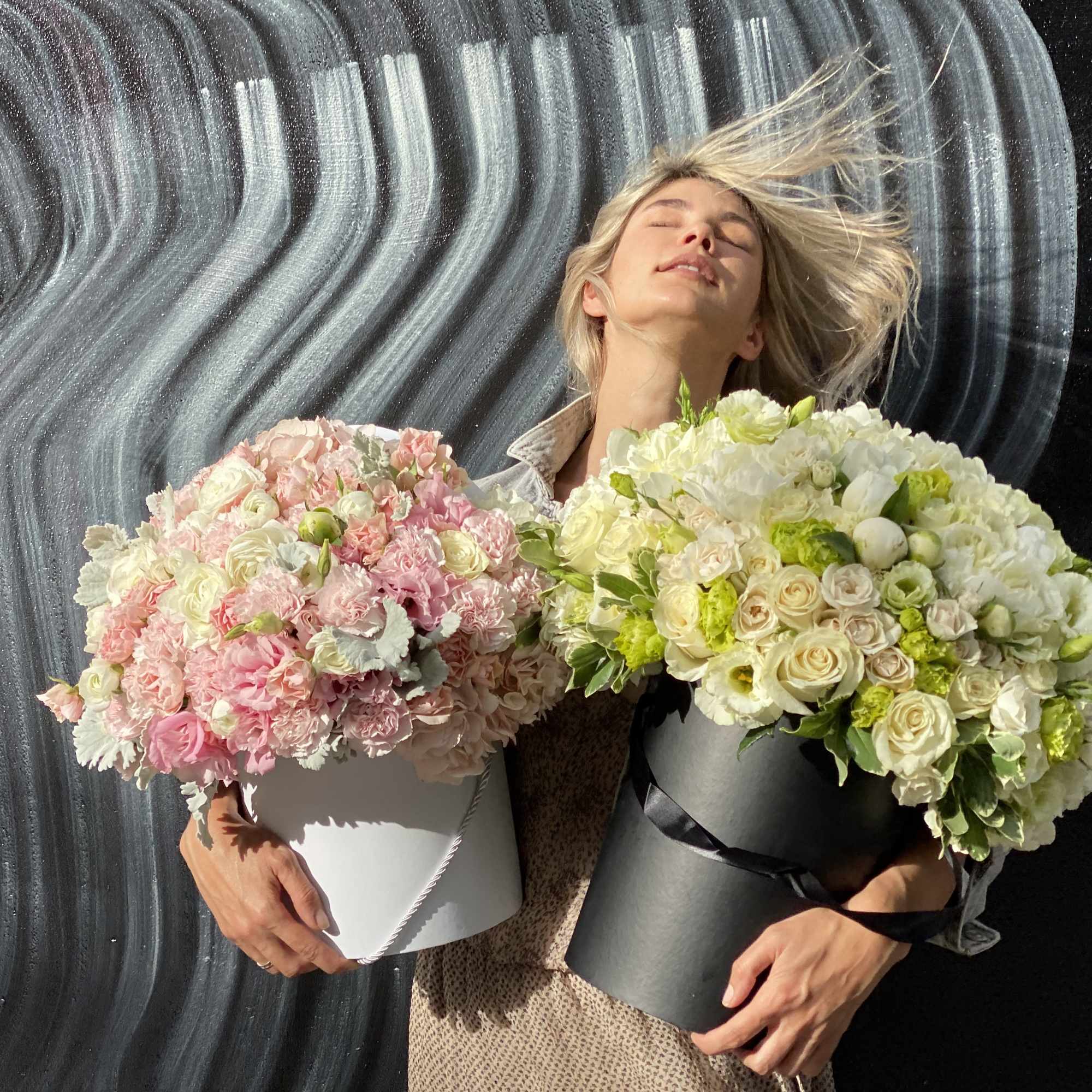 Woman holding two large flower boxes of pink and white blooms
