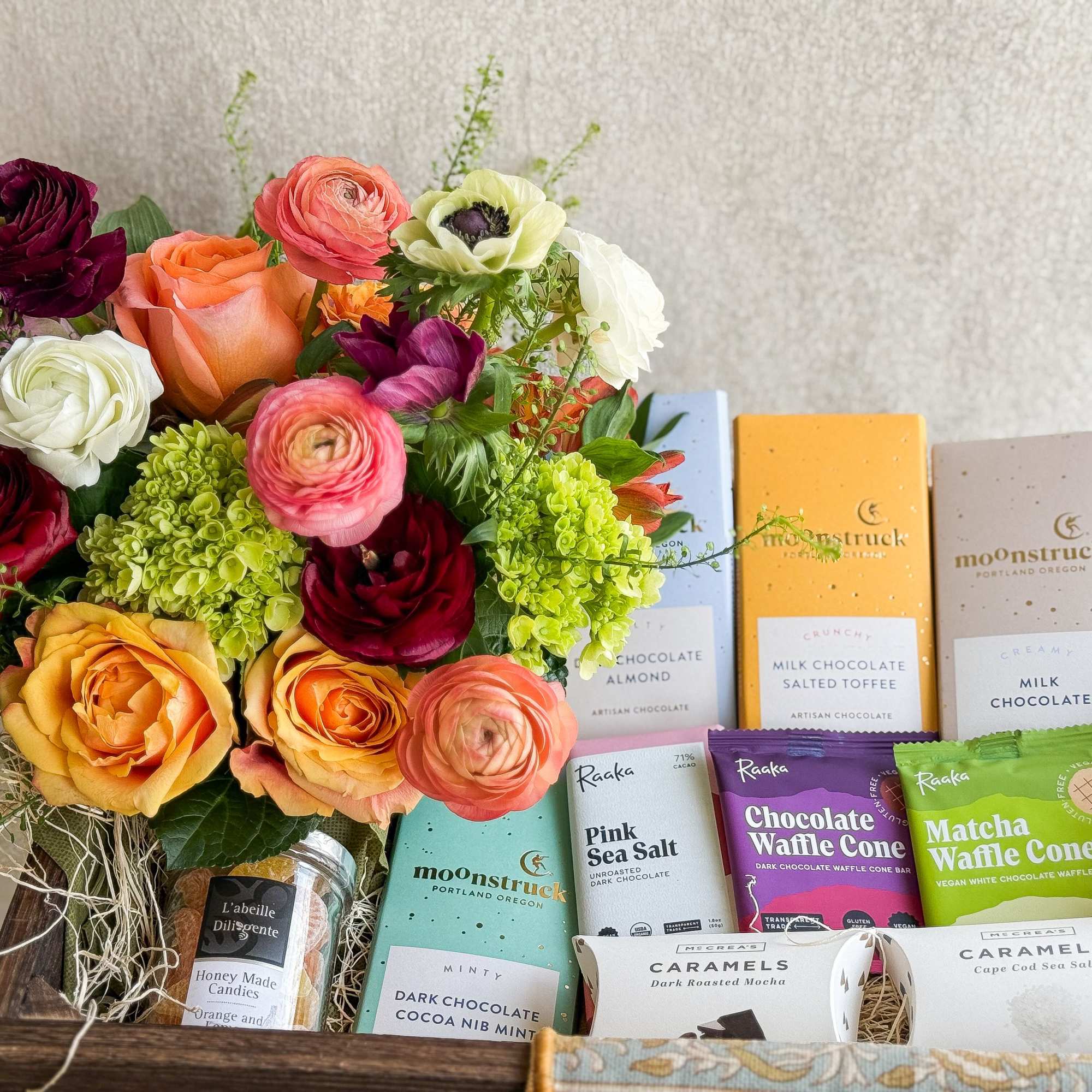 Mixed bouquet beside assorted chocolates and caramels in a wooden gift box