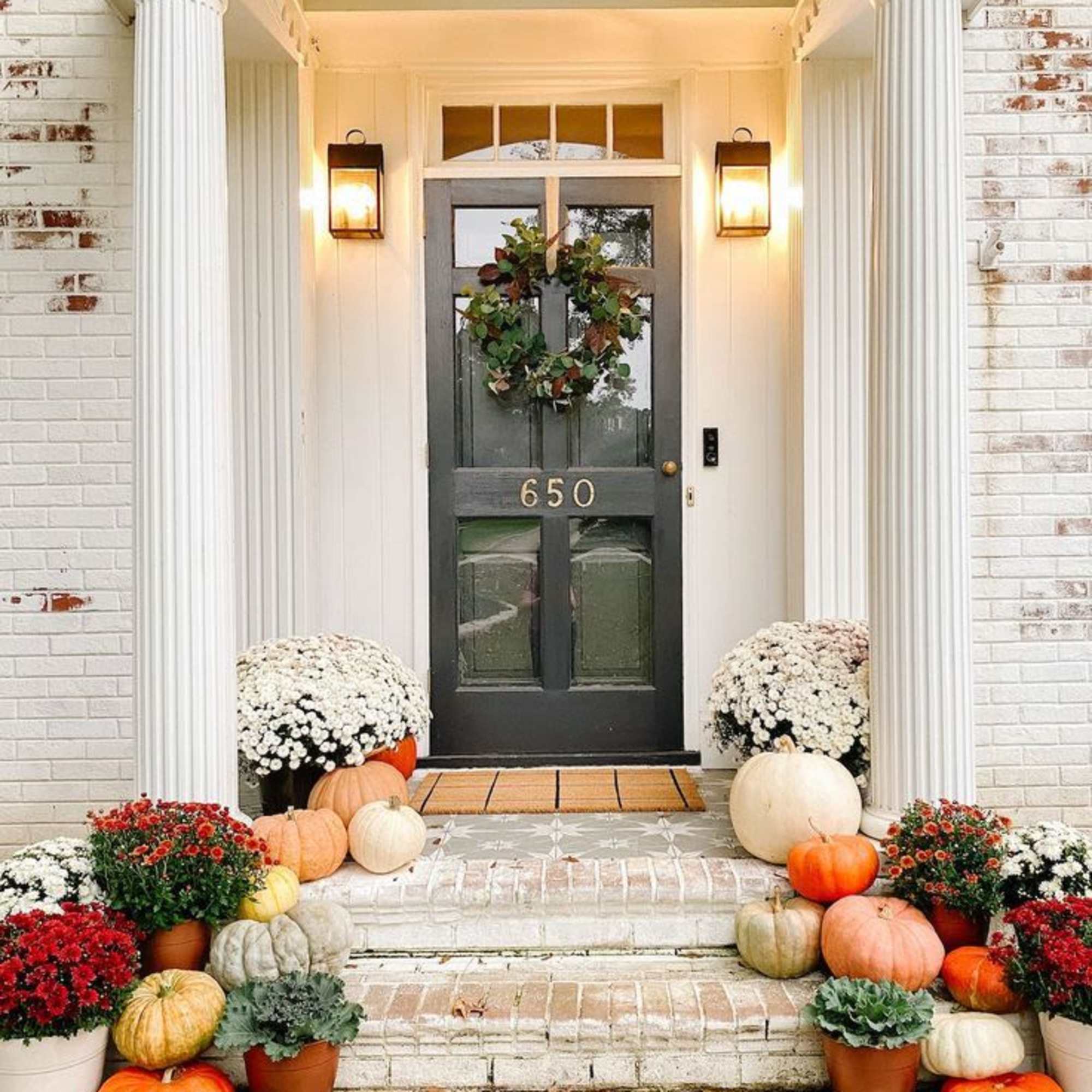 Front porch decorated with pumpkins, potted mums, and a wreath on the door