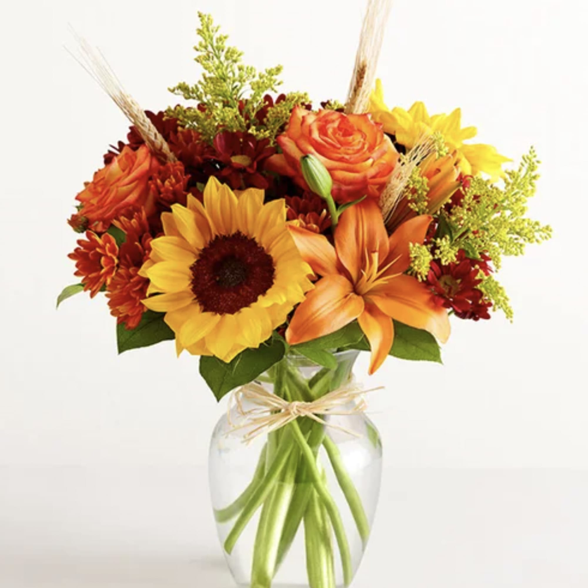 Bouquet of sunflowers, orange lilies, and roses in a clear glass vase