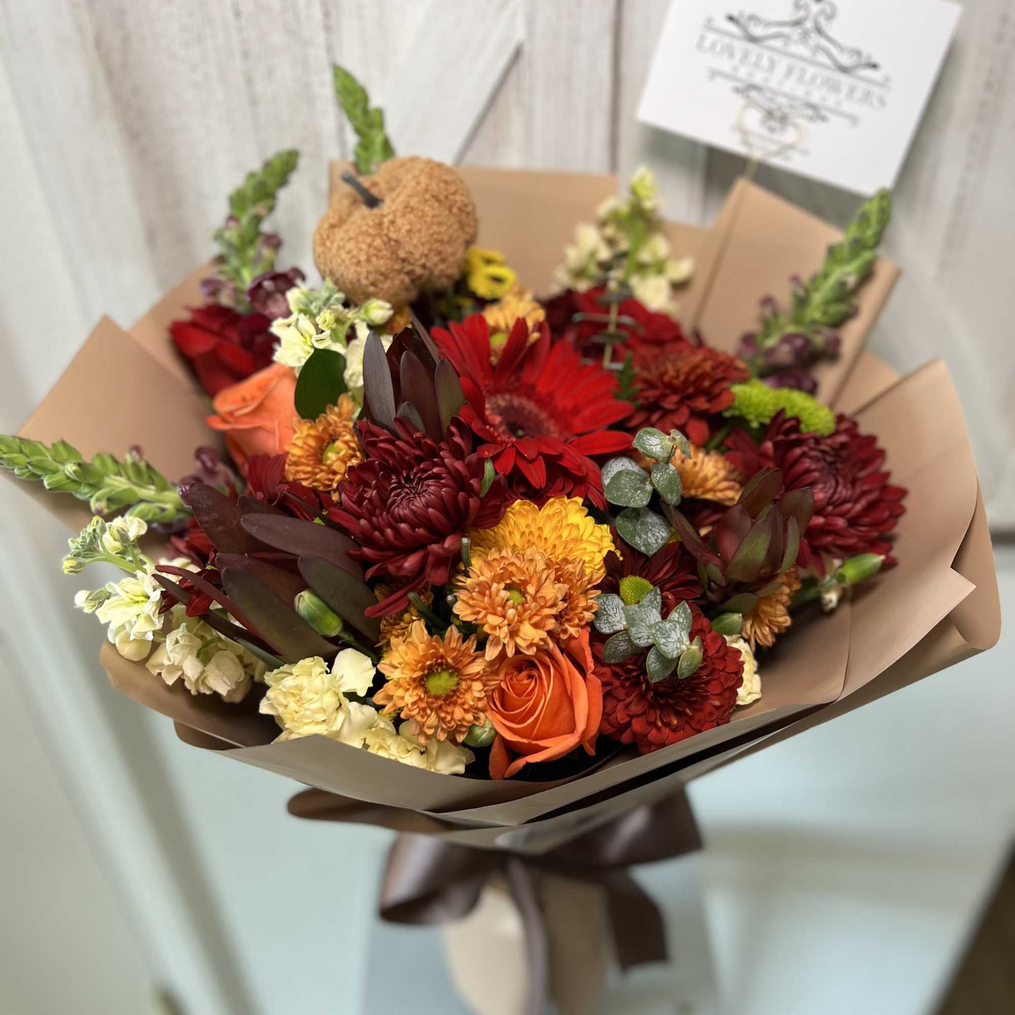 Bouquet of red, orange, and cream flowers wrapped in brown paper