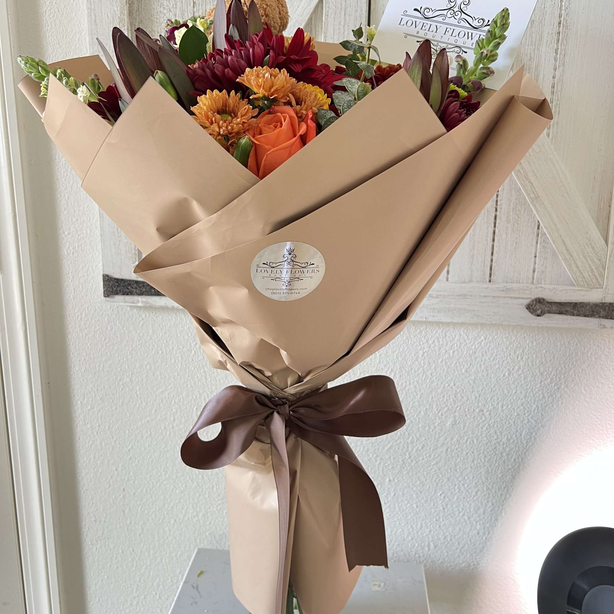 Bouquet of orange and burgundy flowers wrapped in tan paper with a brown ribbon