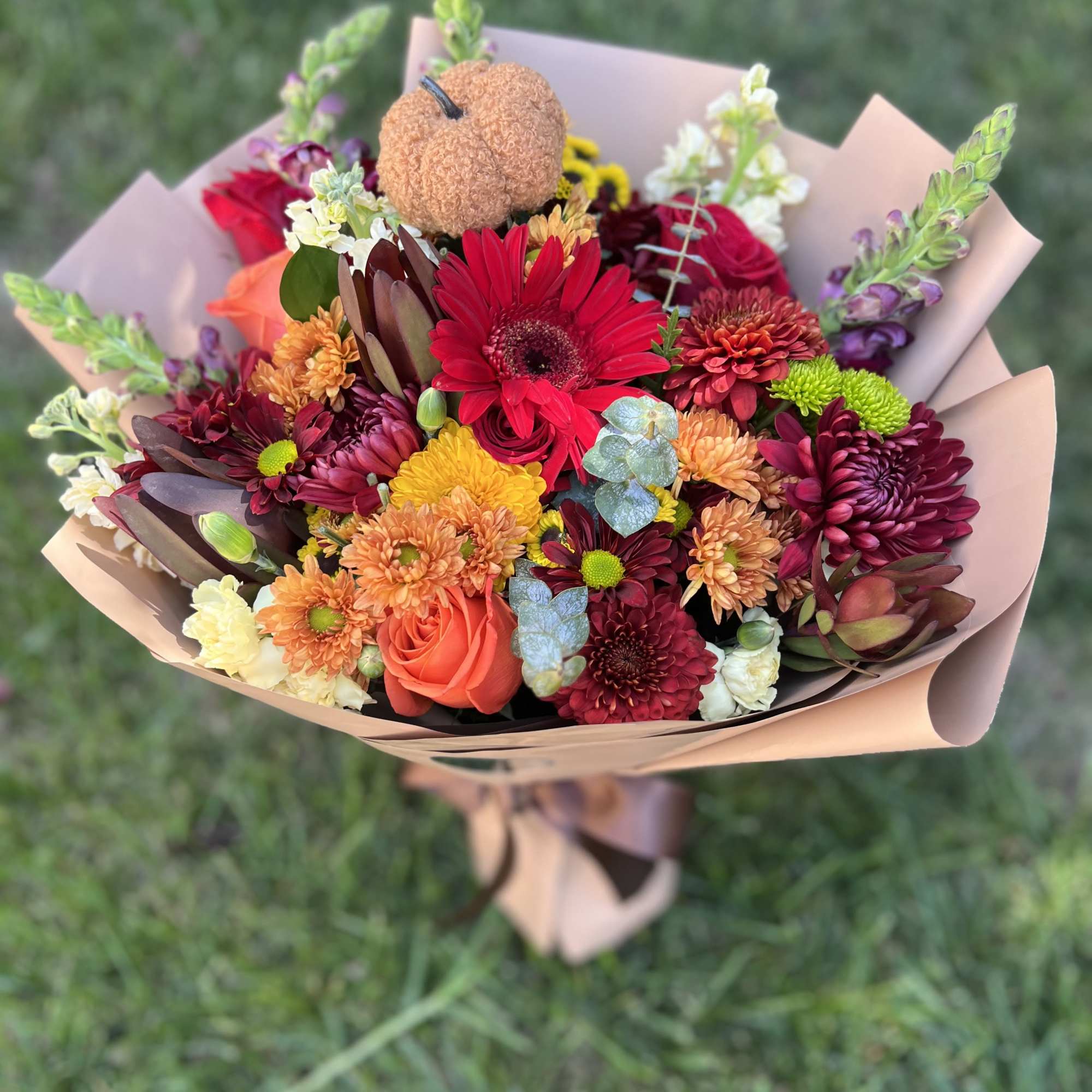 Mixed bouquet of red, orange, and cream flowers wrapped in blush paper