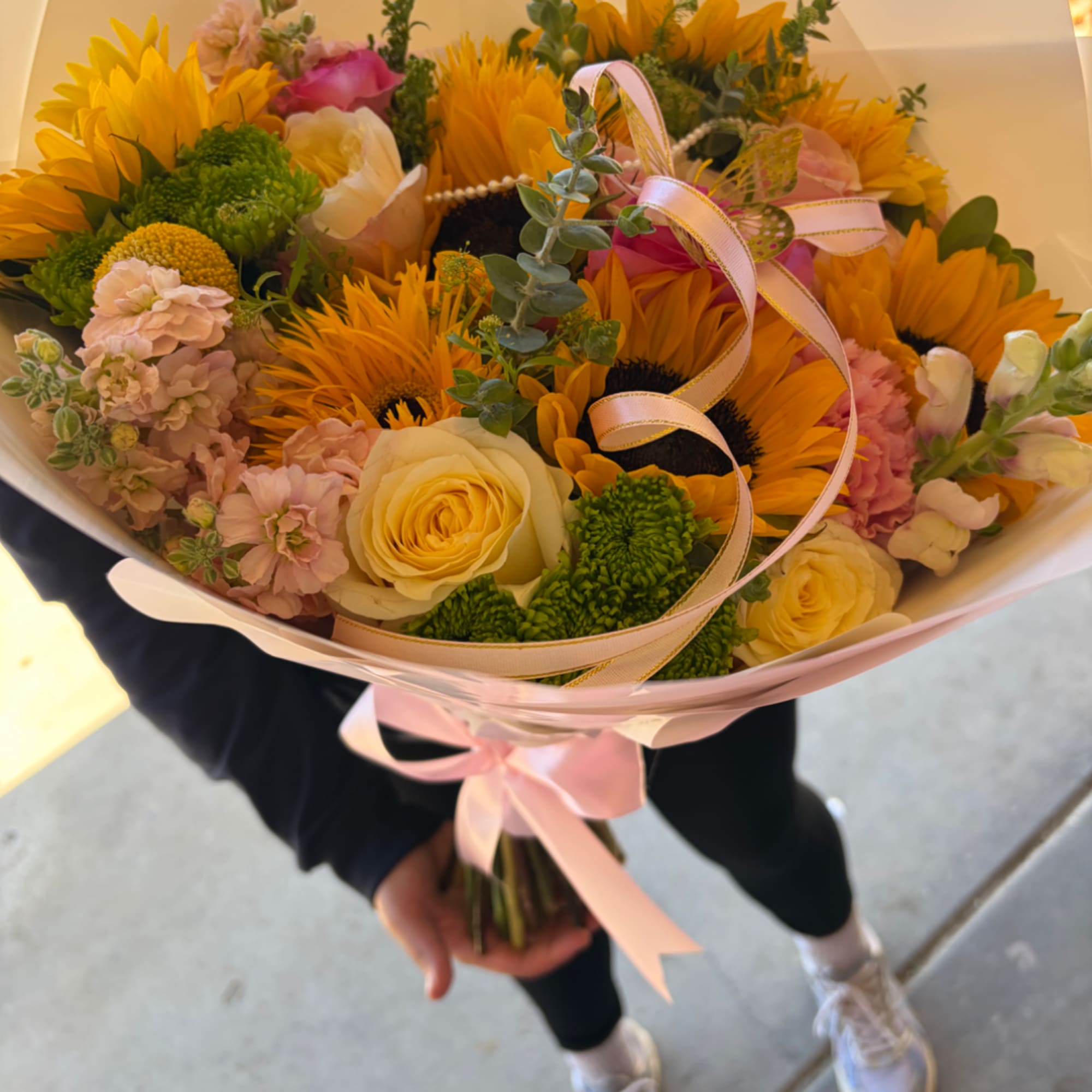 Handheld bouquet of yellow sunflowers and pale roses with pink ribbon