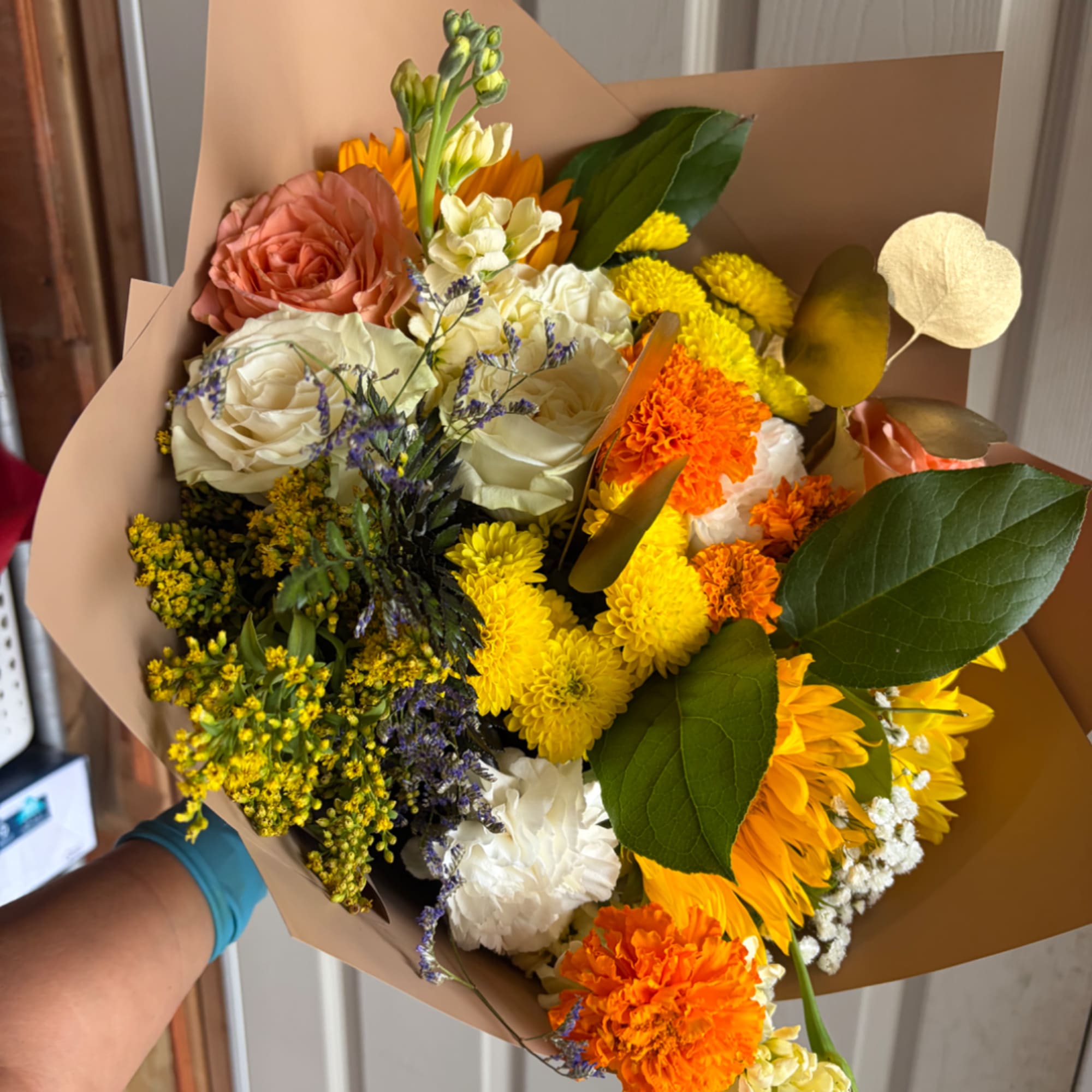 Mixed bouquet with roses, chrysanthemums, sunflowers, and carnations in brown paper