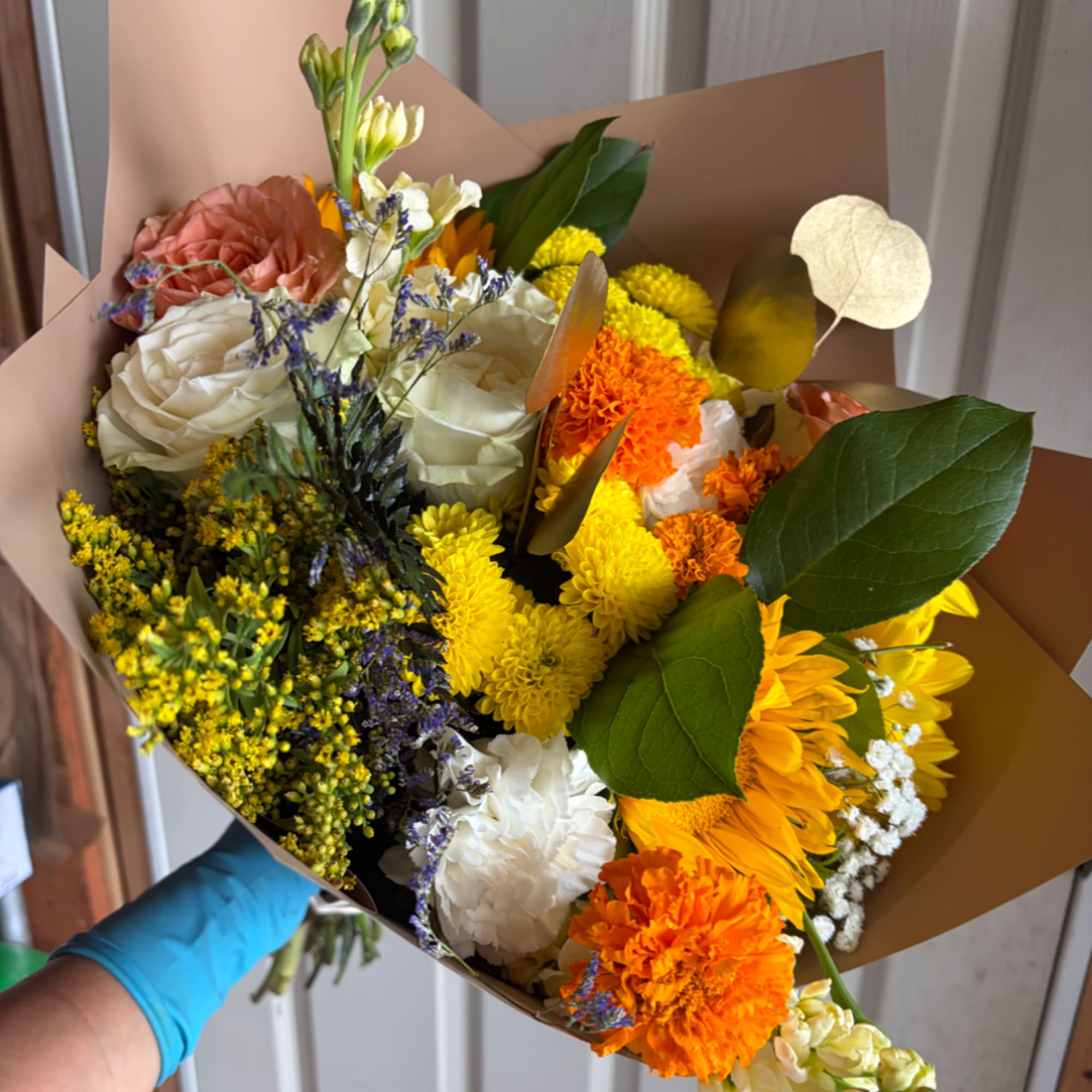 Mixed bouquet of roses, chrysanthemums, and carnations wrapped in brown paper