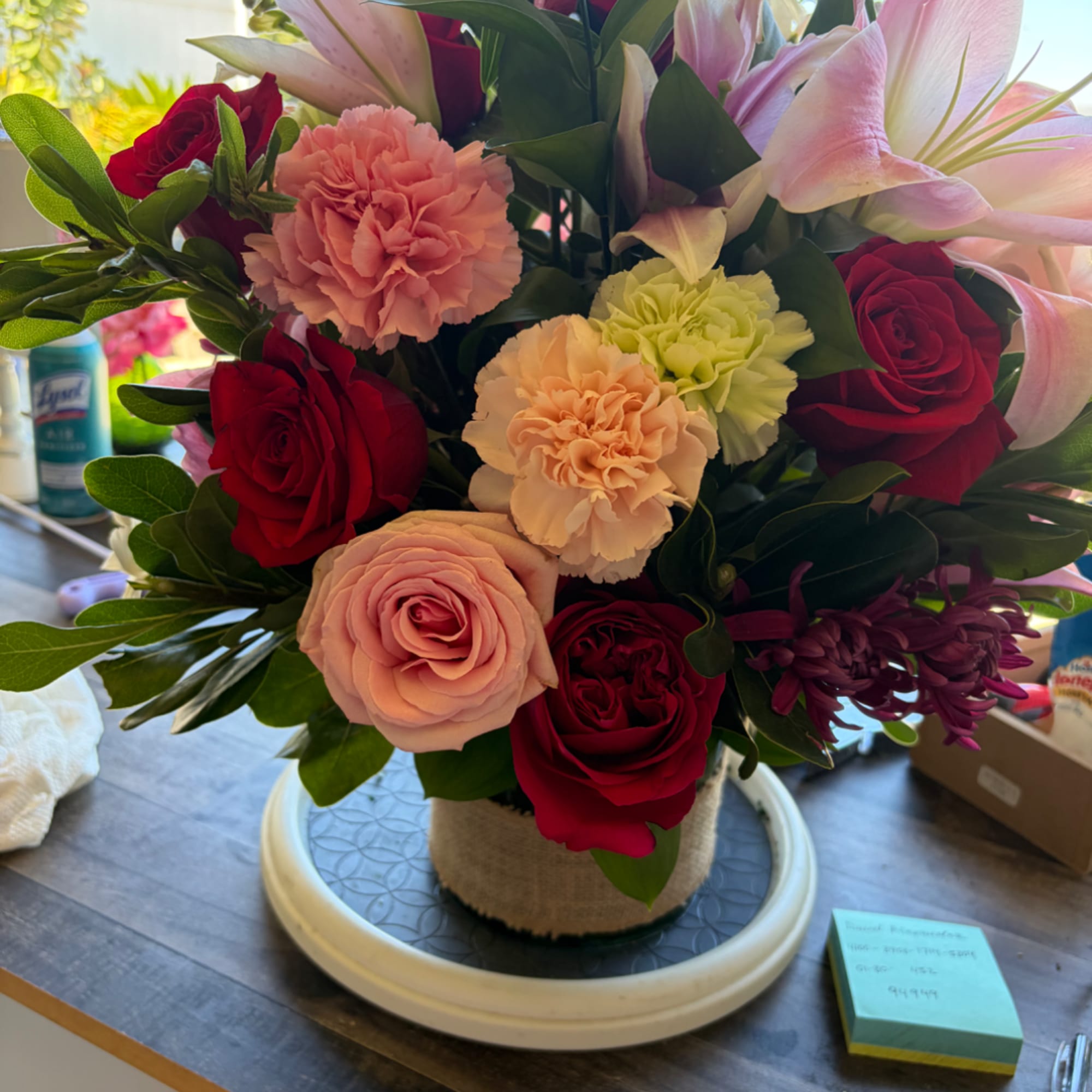Mixed bouquet of red roses, pink lilies, and carnations in a wrapped vase