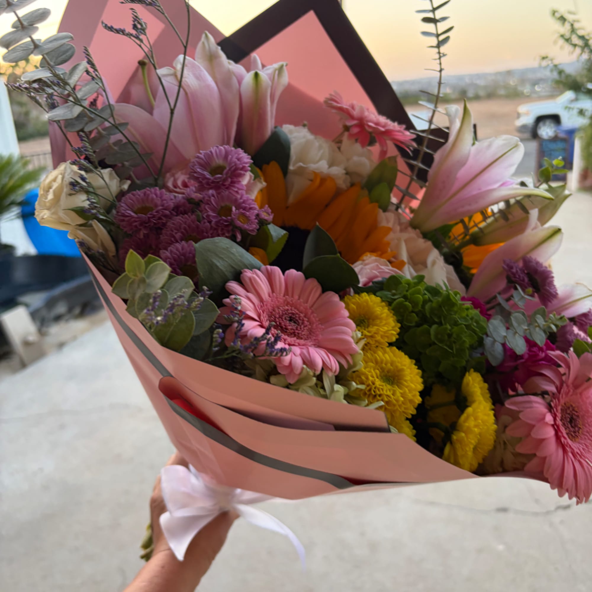 Handheld bouquet of pink lilies, gerbera daisies, and mixed blooms in pink wrap