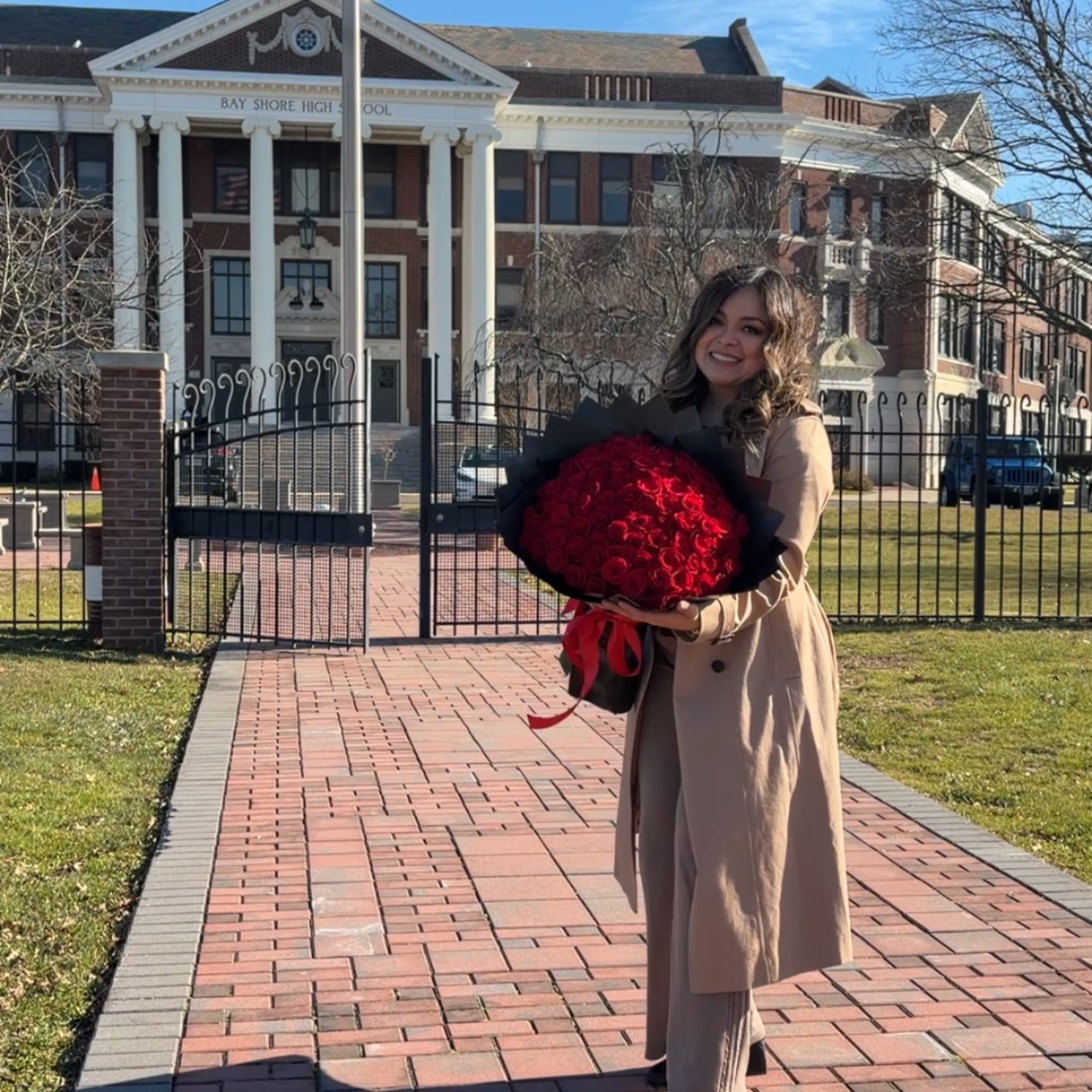 Woman holding a large bouquet of red roses in front of a school building
