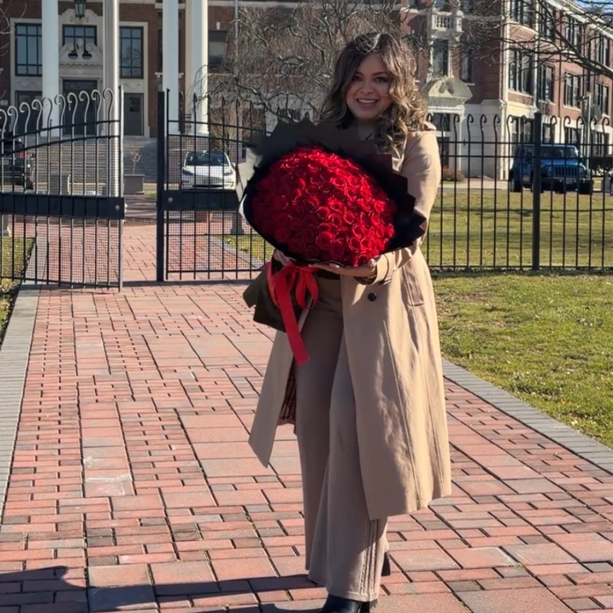 Woman holding a large bouquet of red roses wrapped in black paper