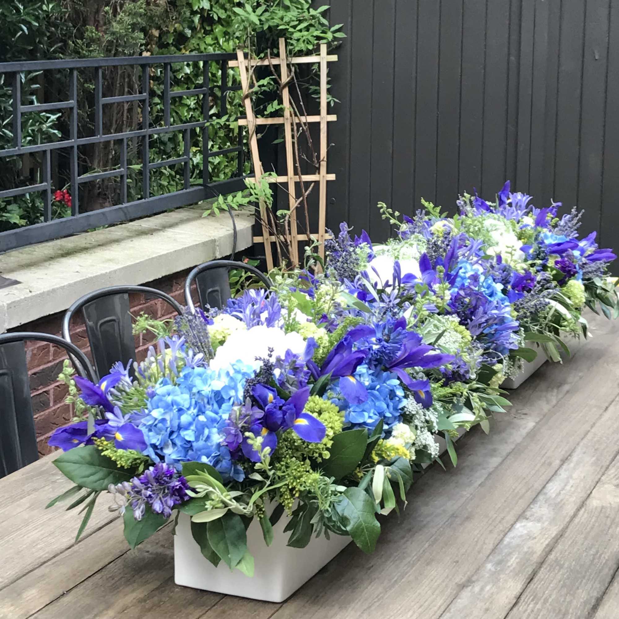 Blue and purple floral centerpiece in a white rectangular container