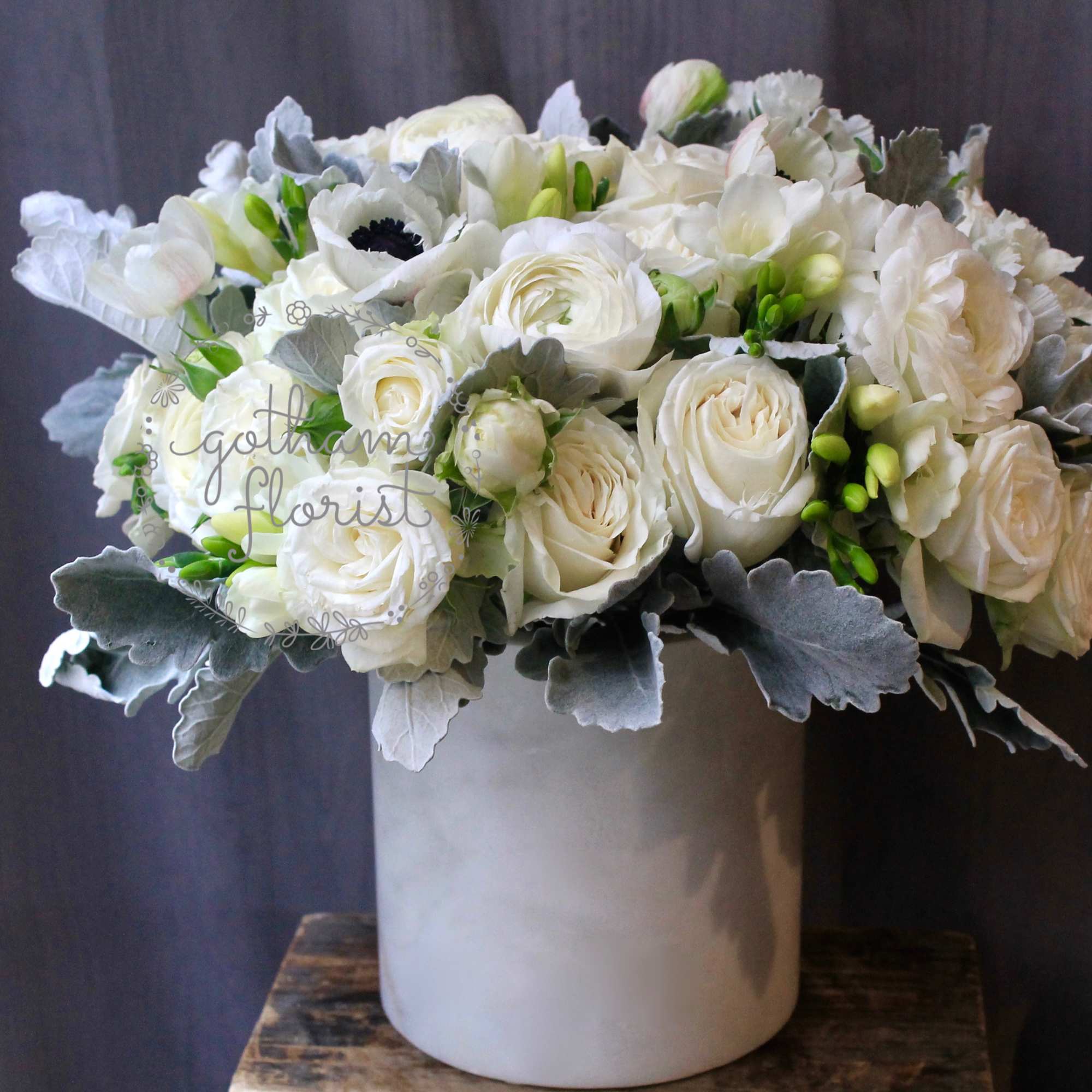 White rose bouquet in a tall gray vase with silver foliage
