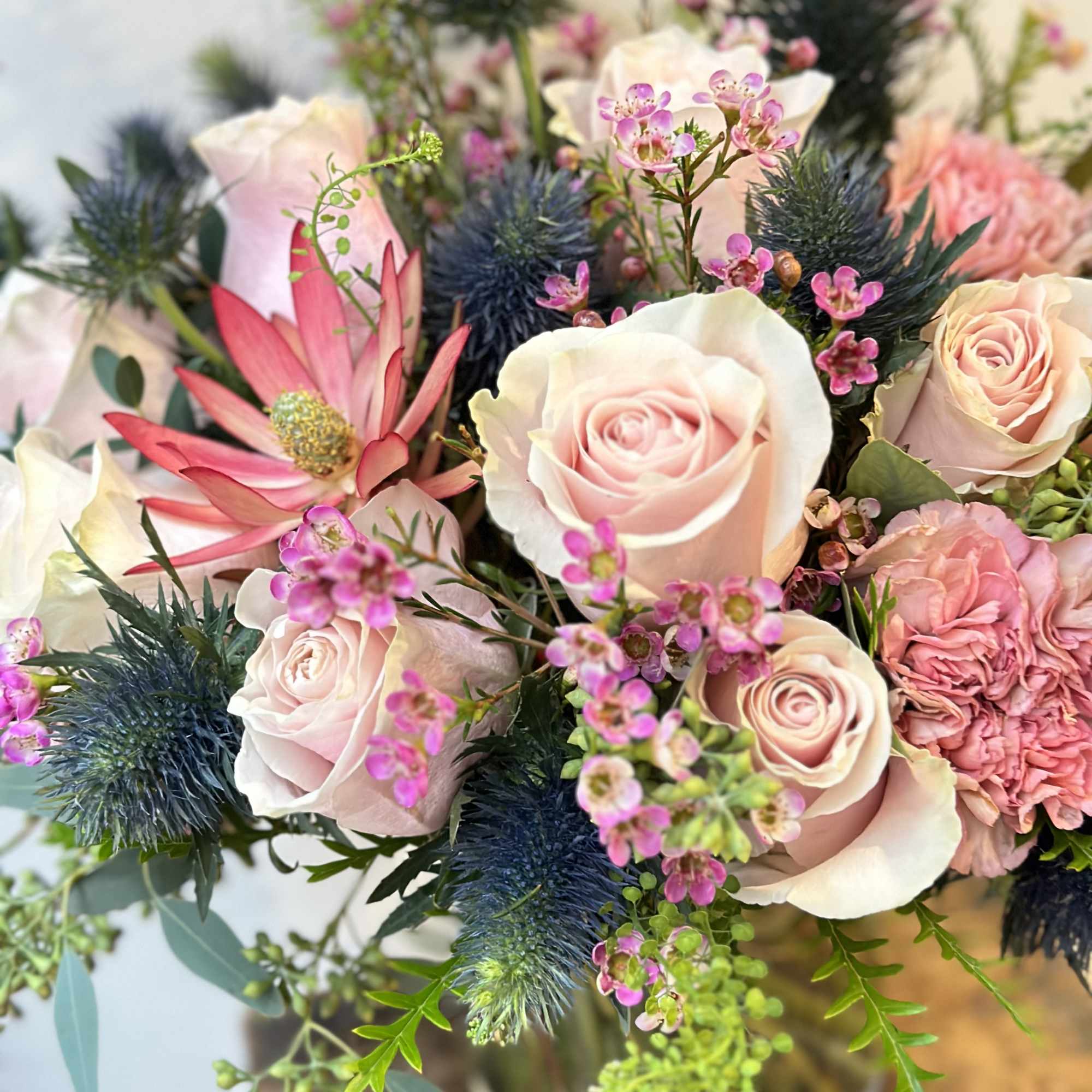 Bouquet of pale pink roses and pink blooms with blue thistle in a vase