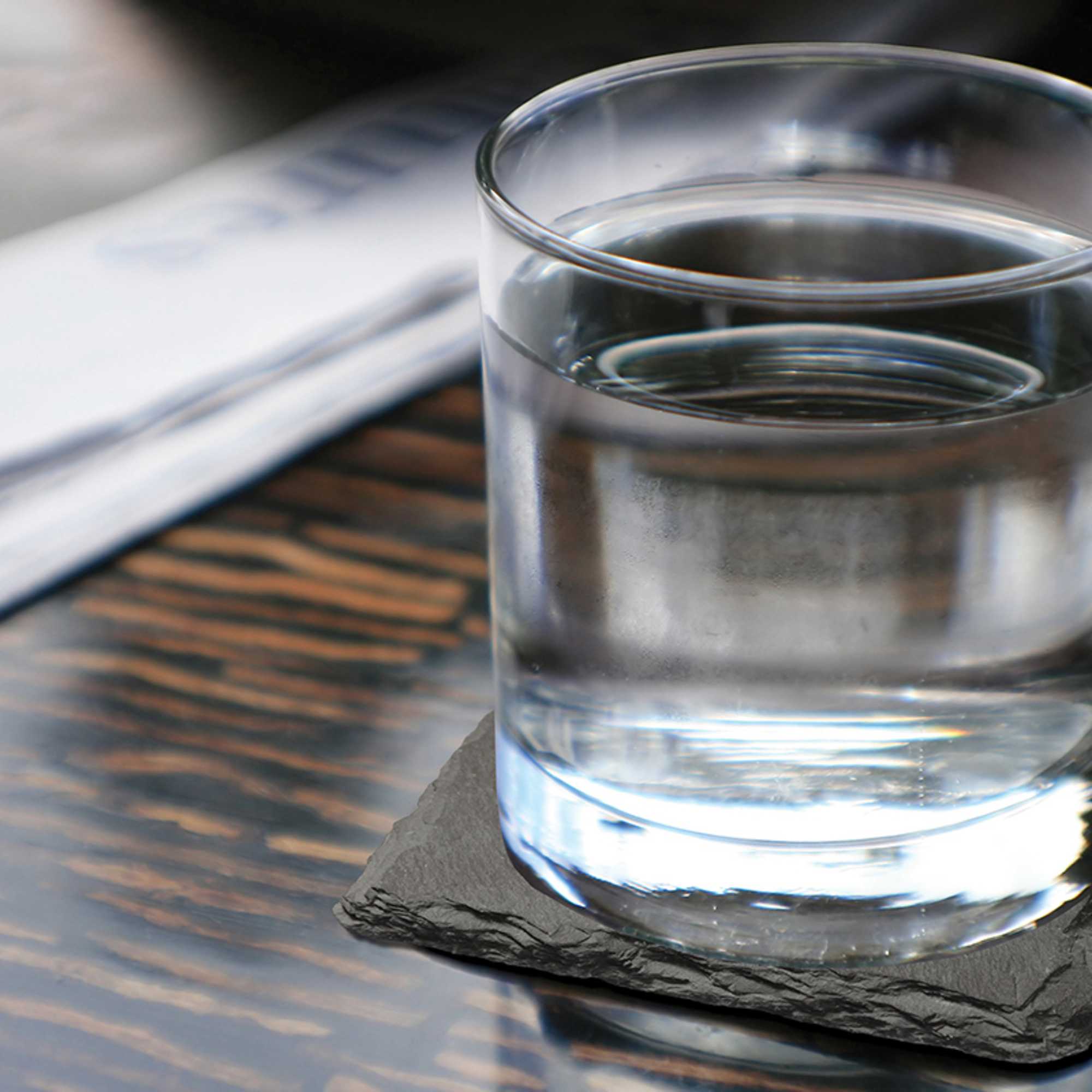 A clear glass of water on a dark coaster