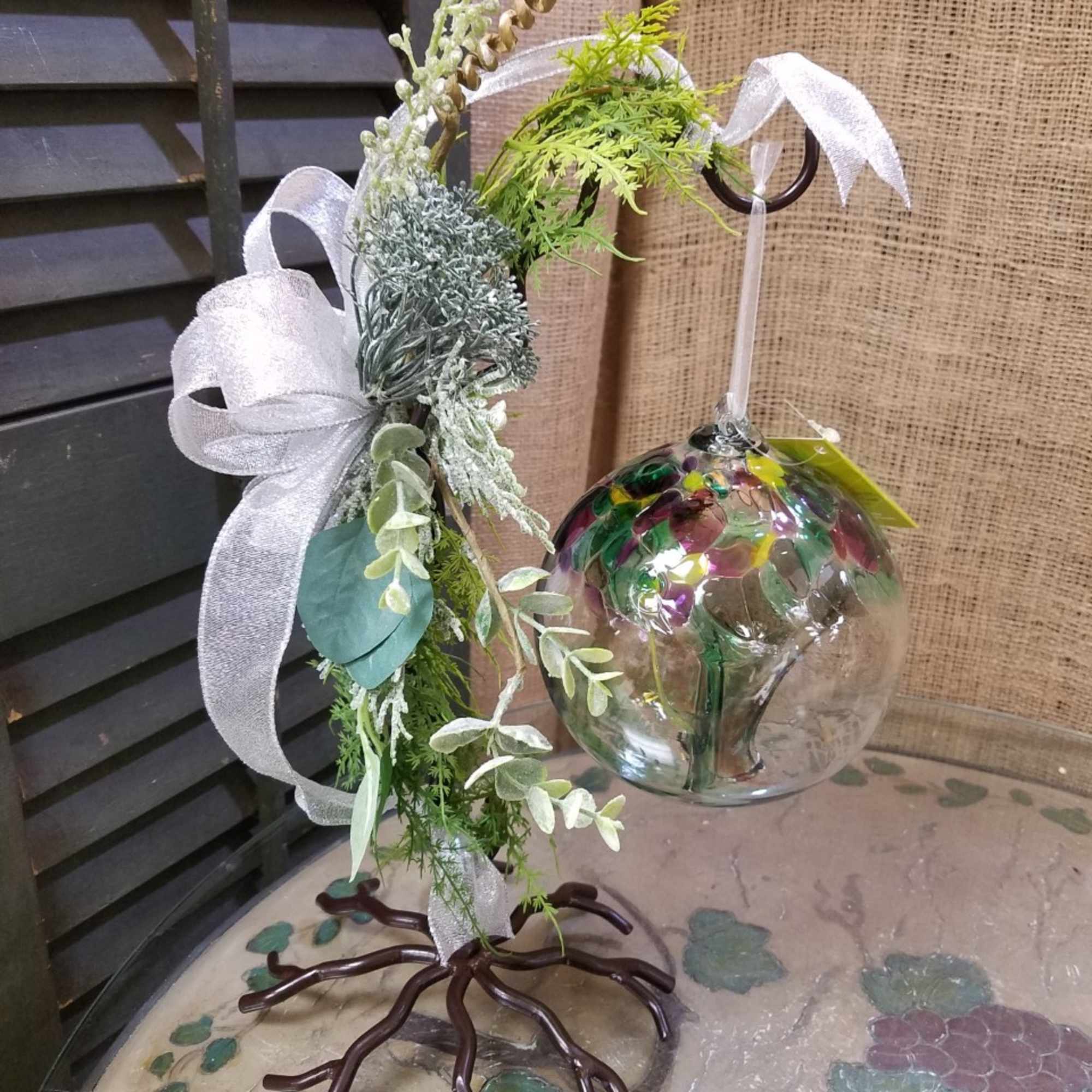 Decorative hanging glass ornament with faux greenery and a white ribbon