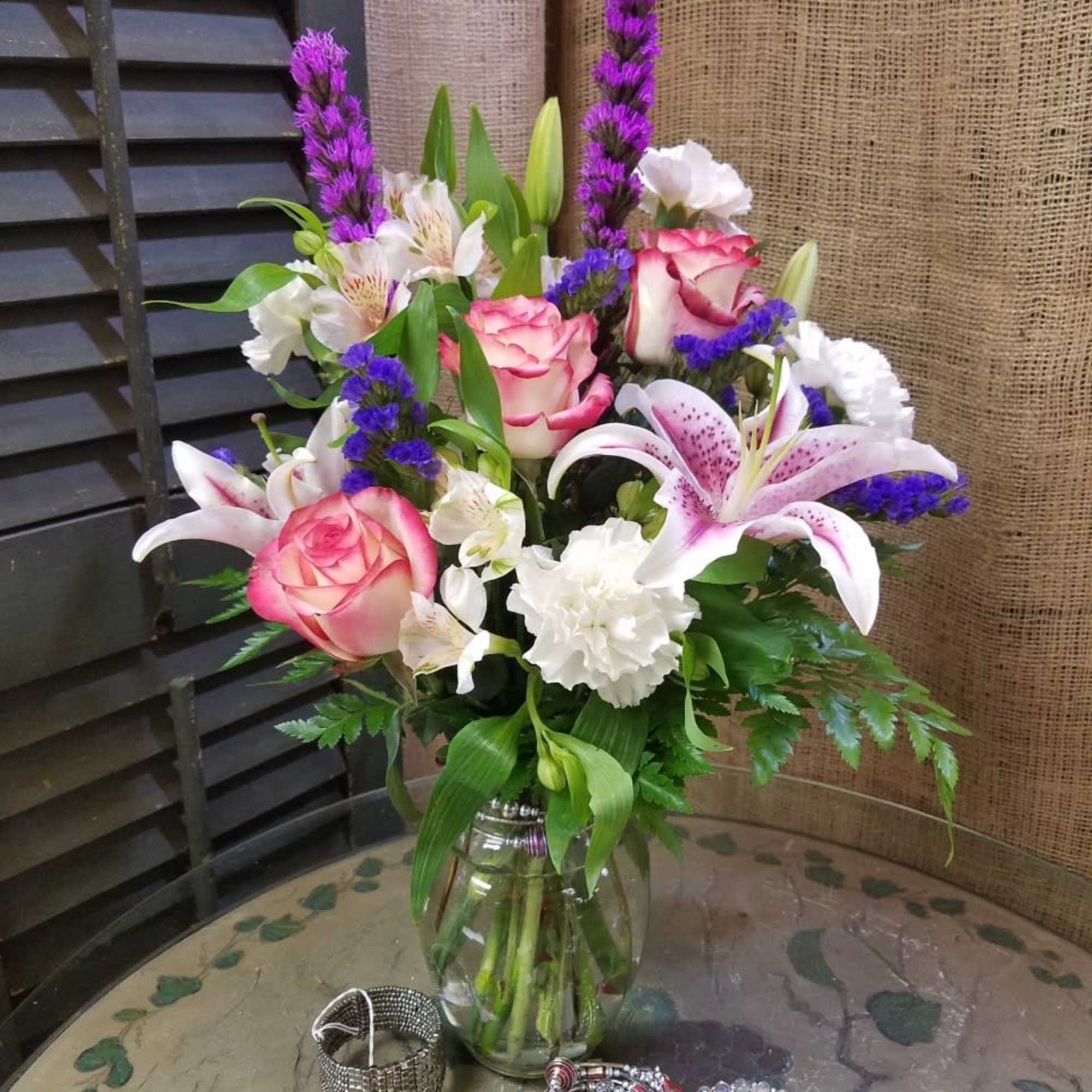 Mixed bouquet of pink roses, lilies, and purple spikes in a glass vase