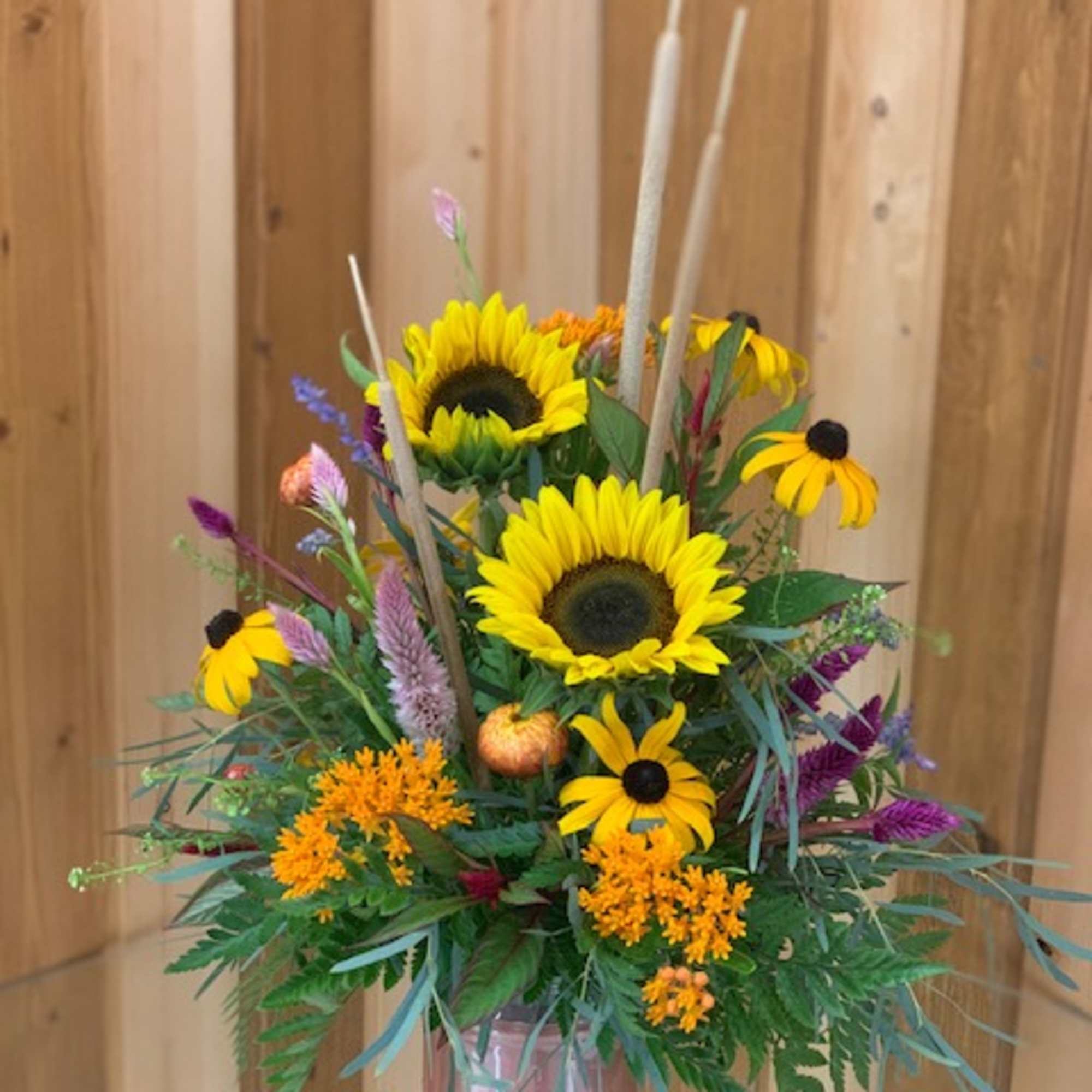 Sunflower arrangement with orange and purple accents in a pink vase