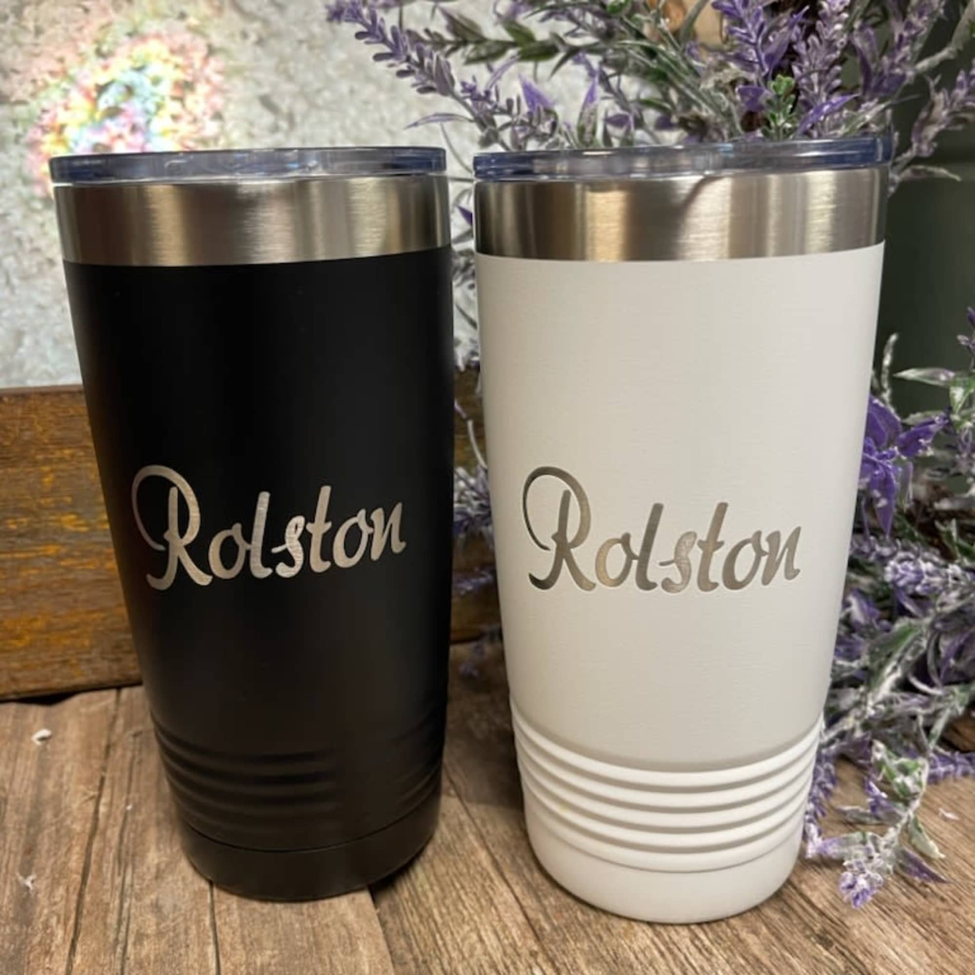 Two personalized tumblers with purple floral stems behind them