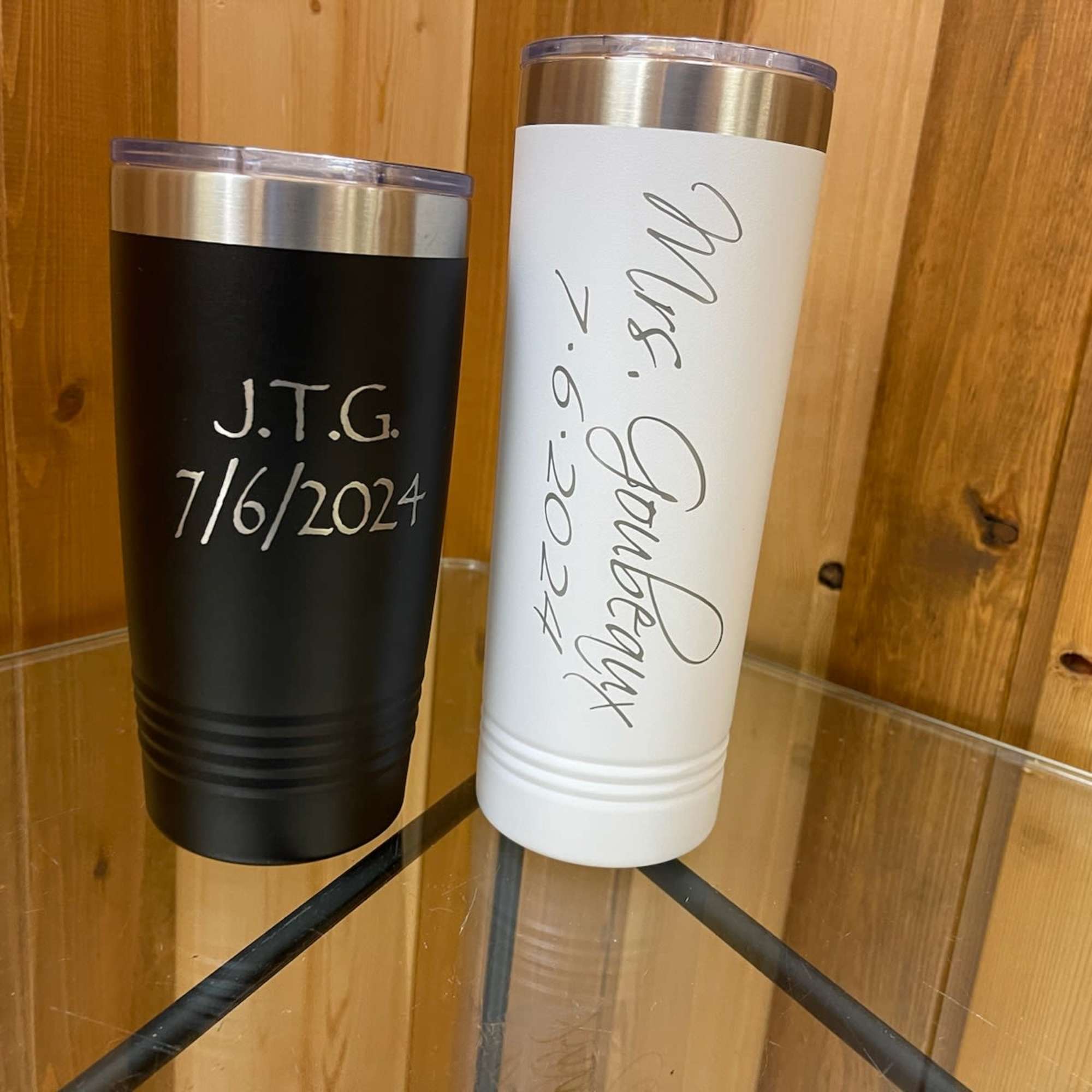 Two personalized insulated tumblers, one black and one white, on a glass table.