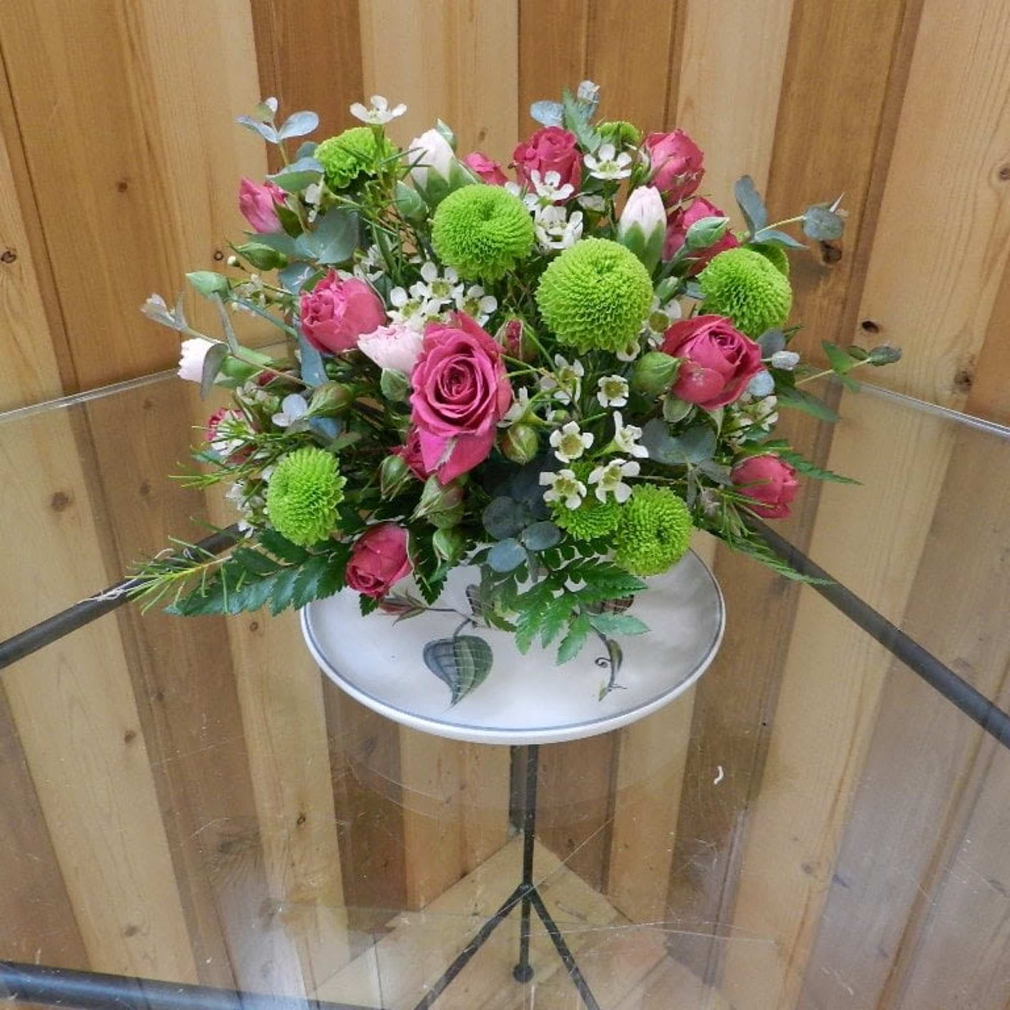 Pink roses and green pom-pom flowers in a low arrangement on a stand