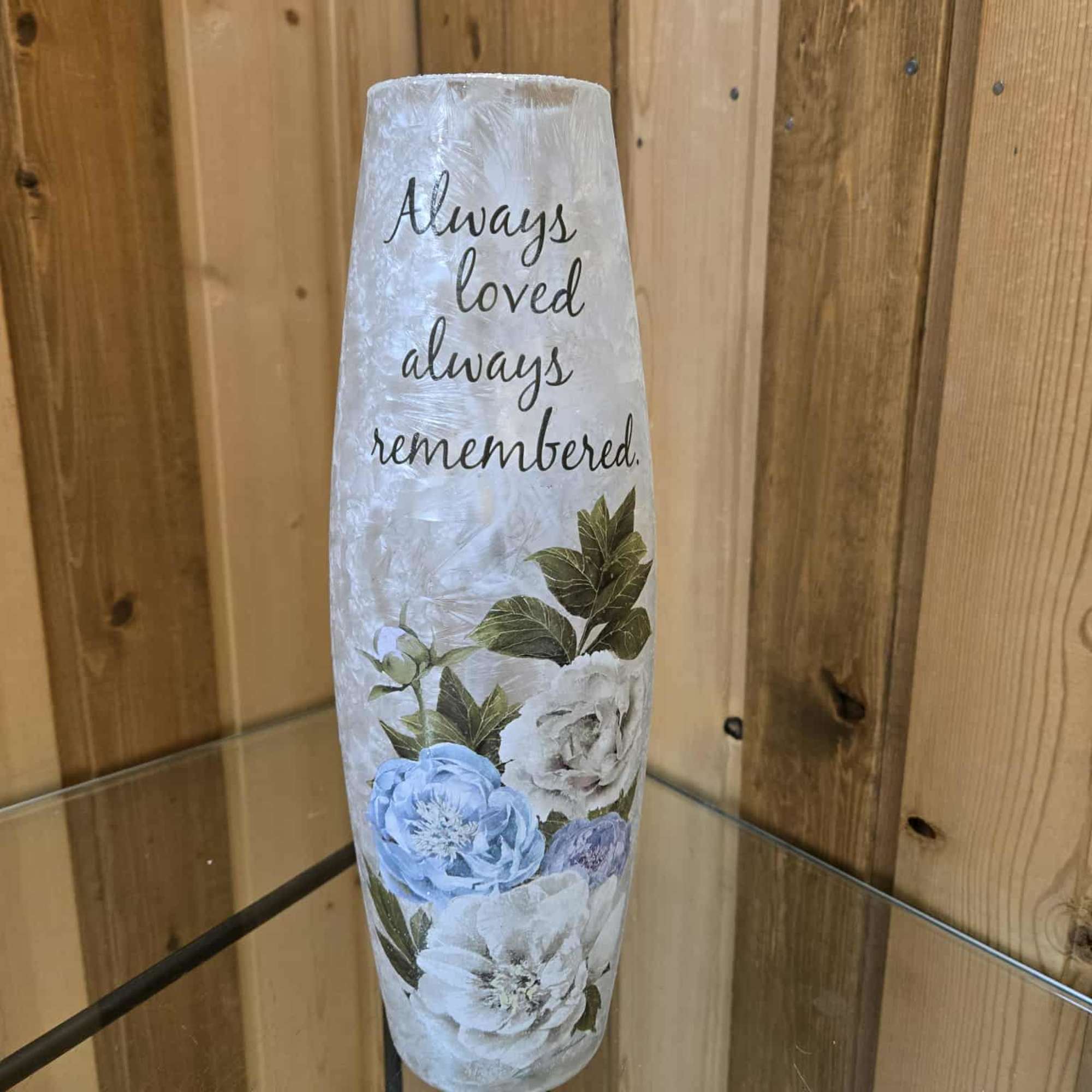 Tall white memorial vase with blue and white flowers and the words "Always loved, always remembered."
