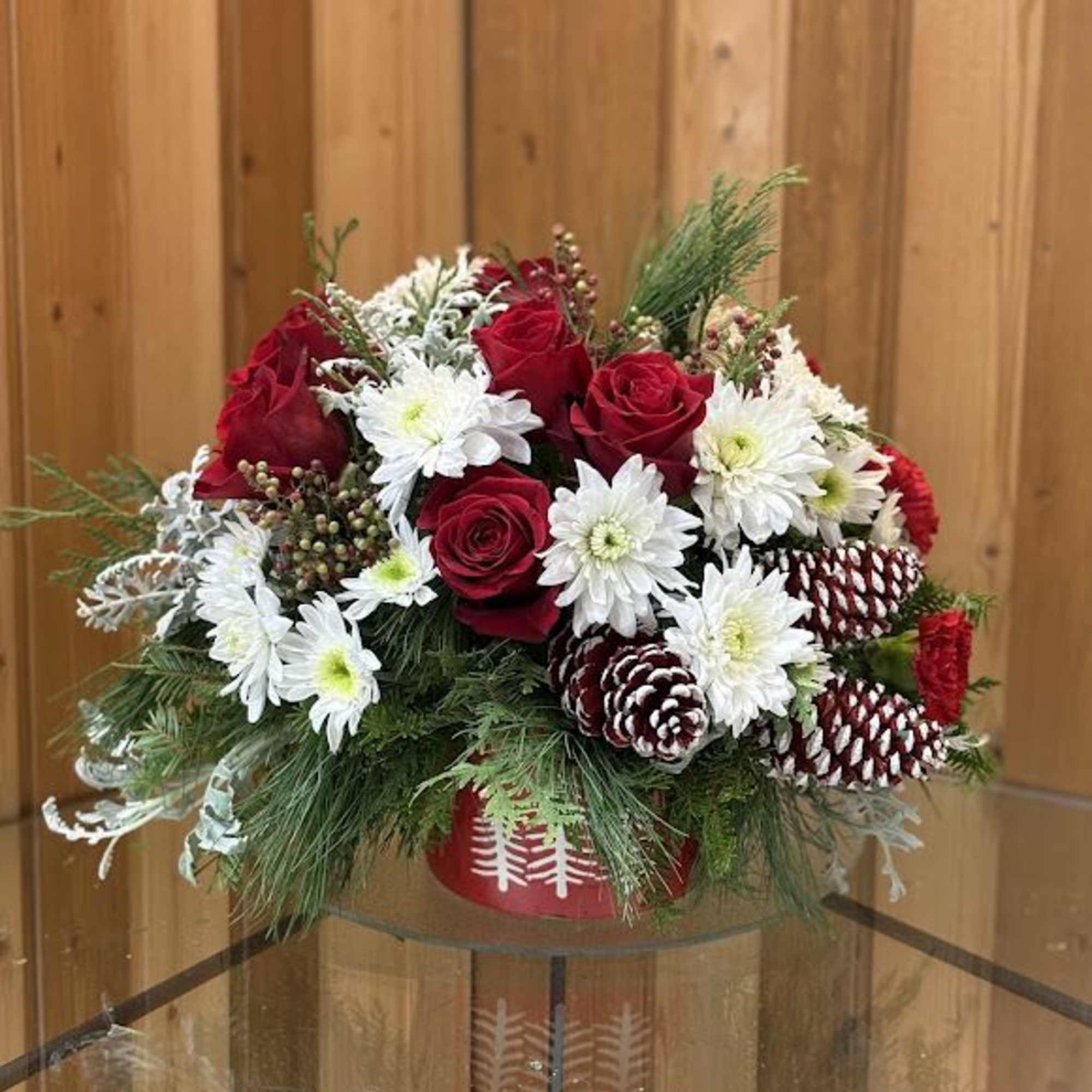 Red roses and white daisies arranged in a red container with pinecones