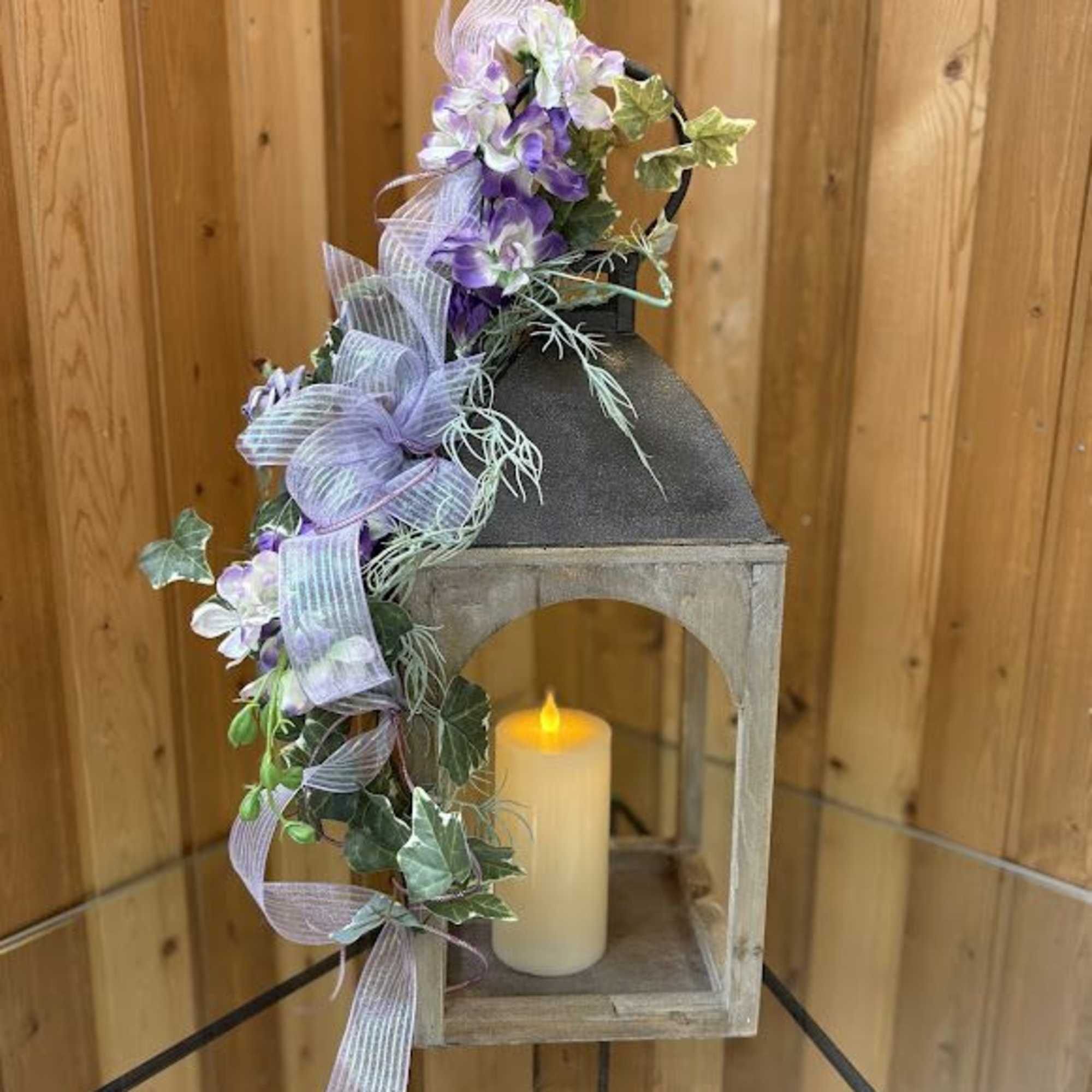 Lavender floral garland draped over a lantern with a candle inside.