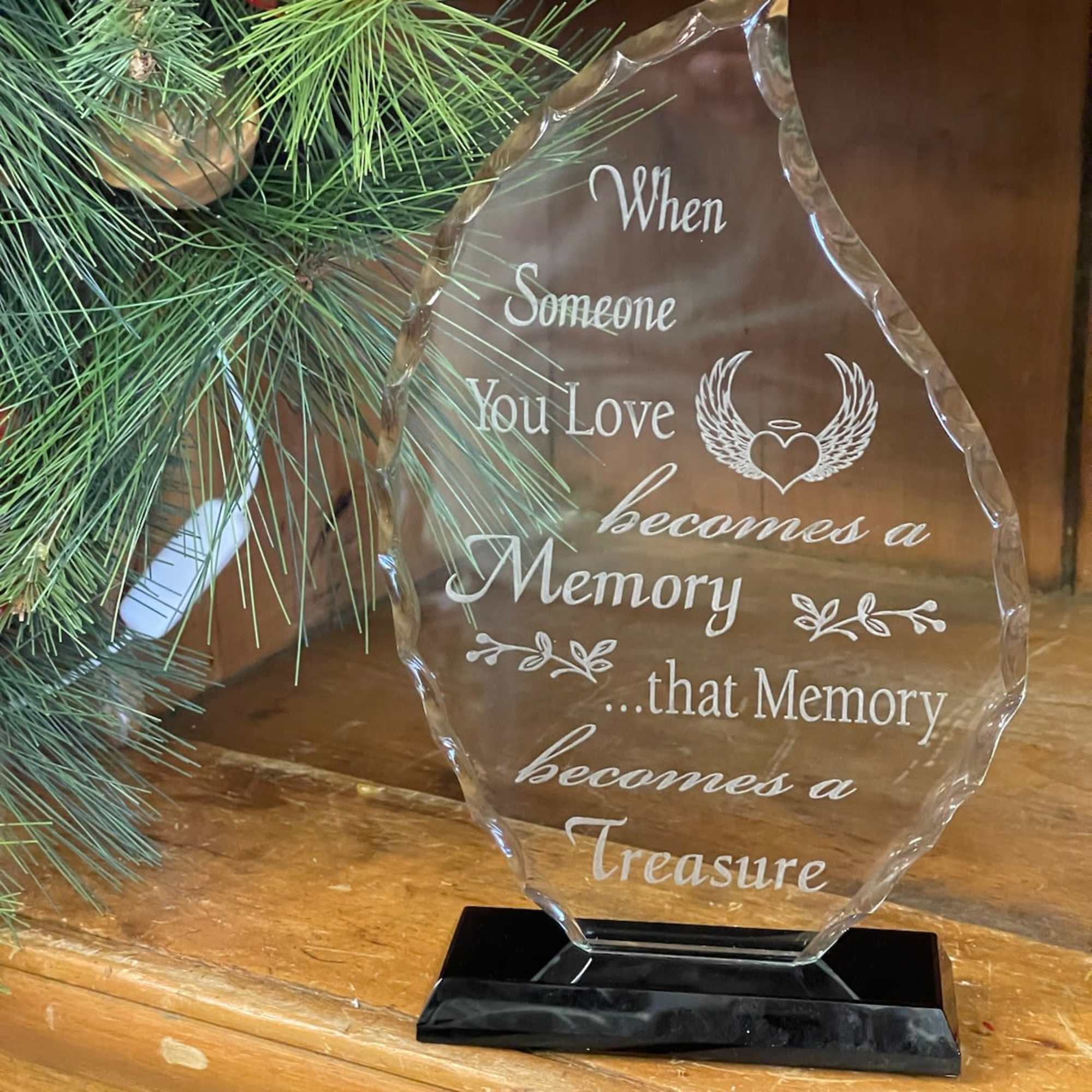 Clear memorial plaque on a black base beside pine branches and red berries