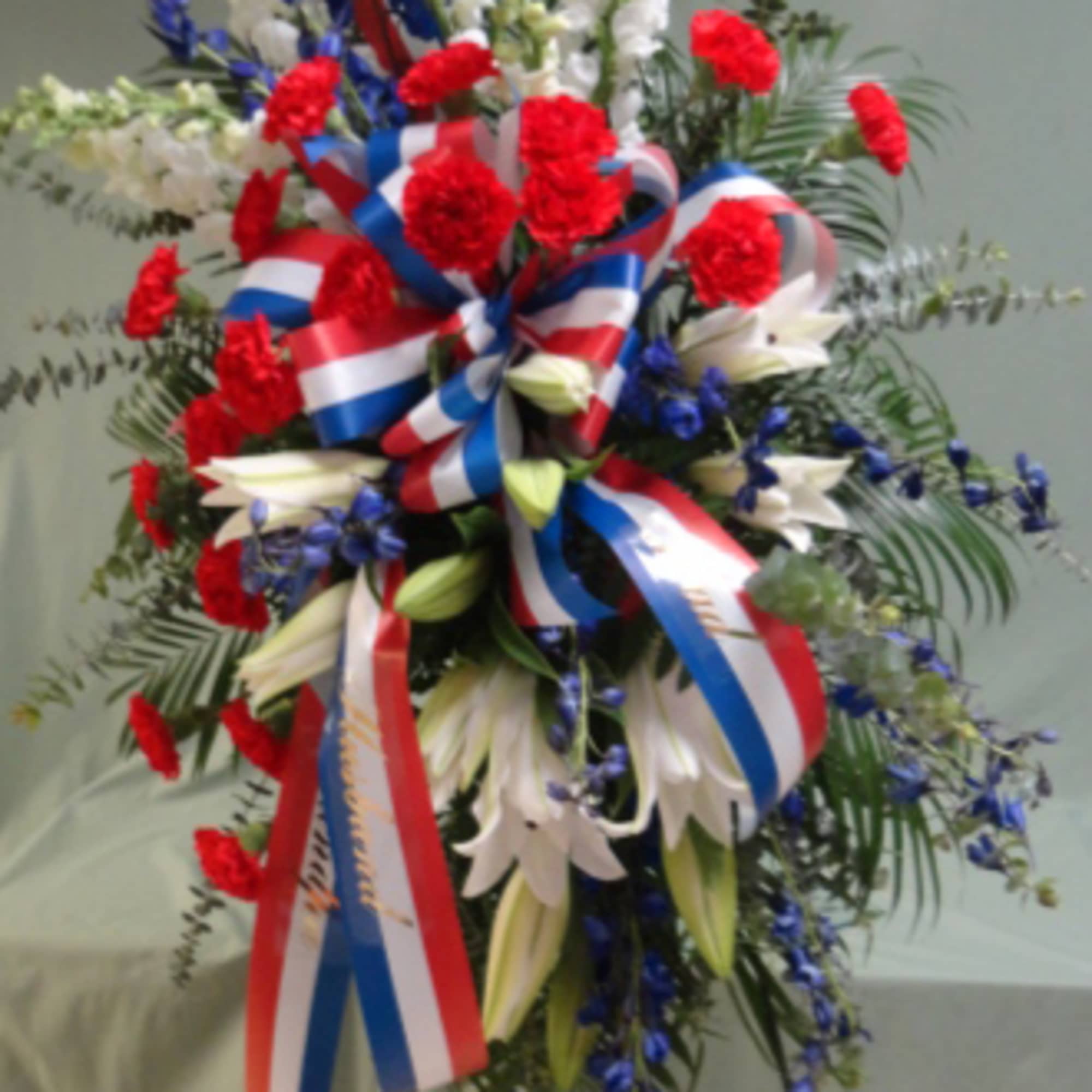 Tall standing floral spray with red, white, and blue flowers and ribbons