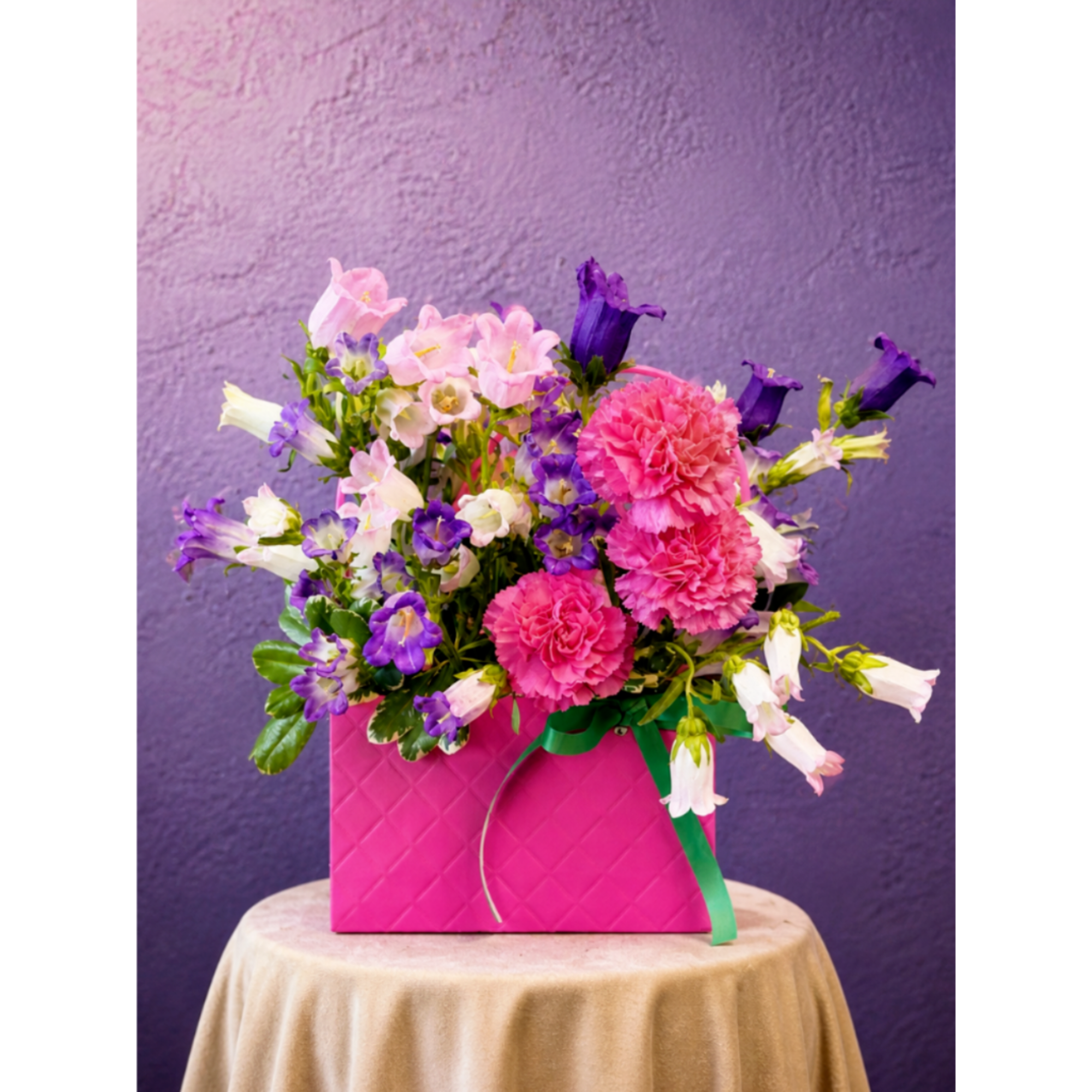 Pink and purple mixed flowers arranged in a bright pink box with a green ribbon