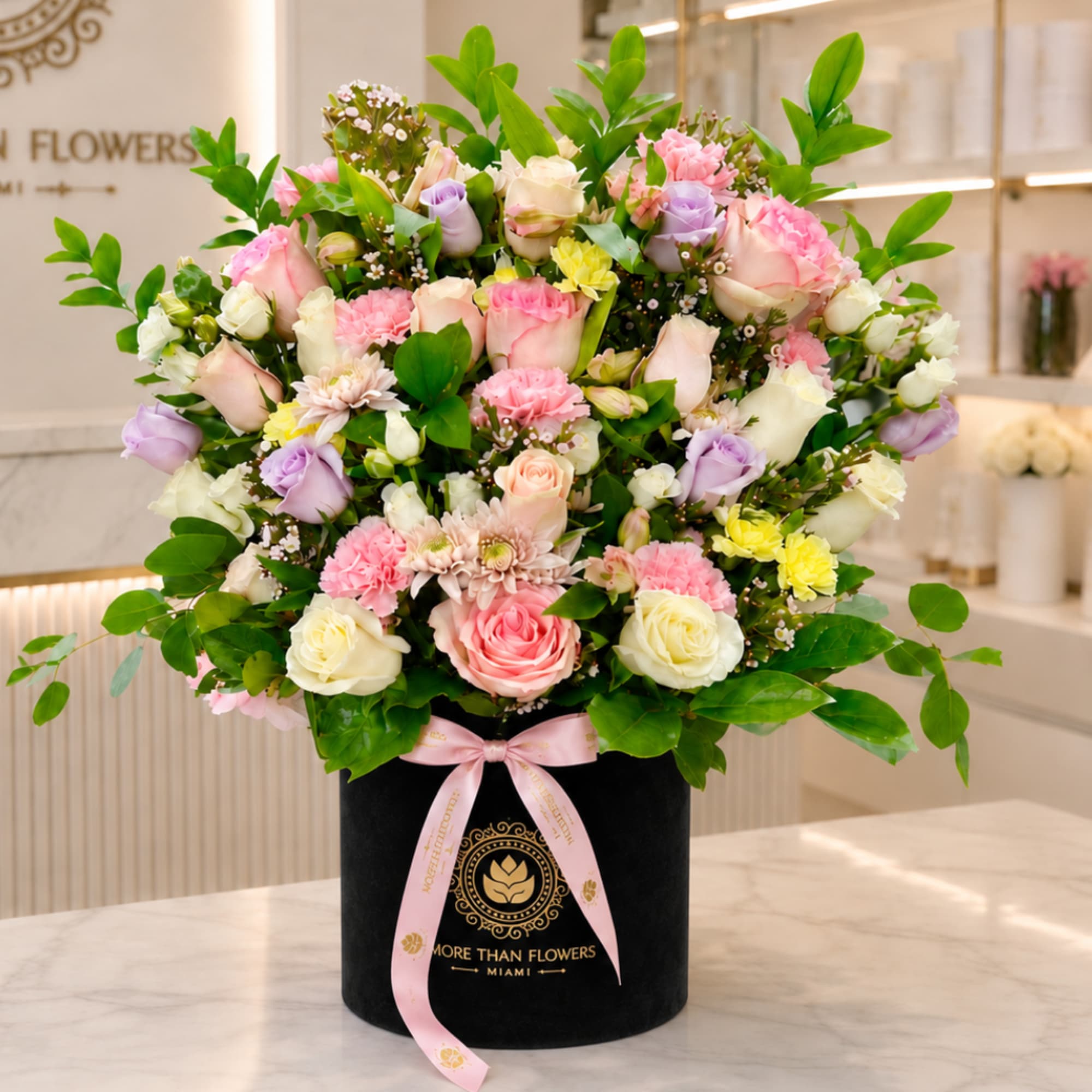 Mixed pink, white, and lavender flowers in a black hatbox with a pink ribbon