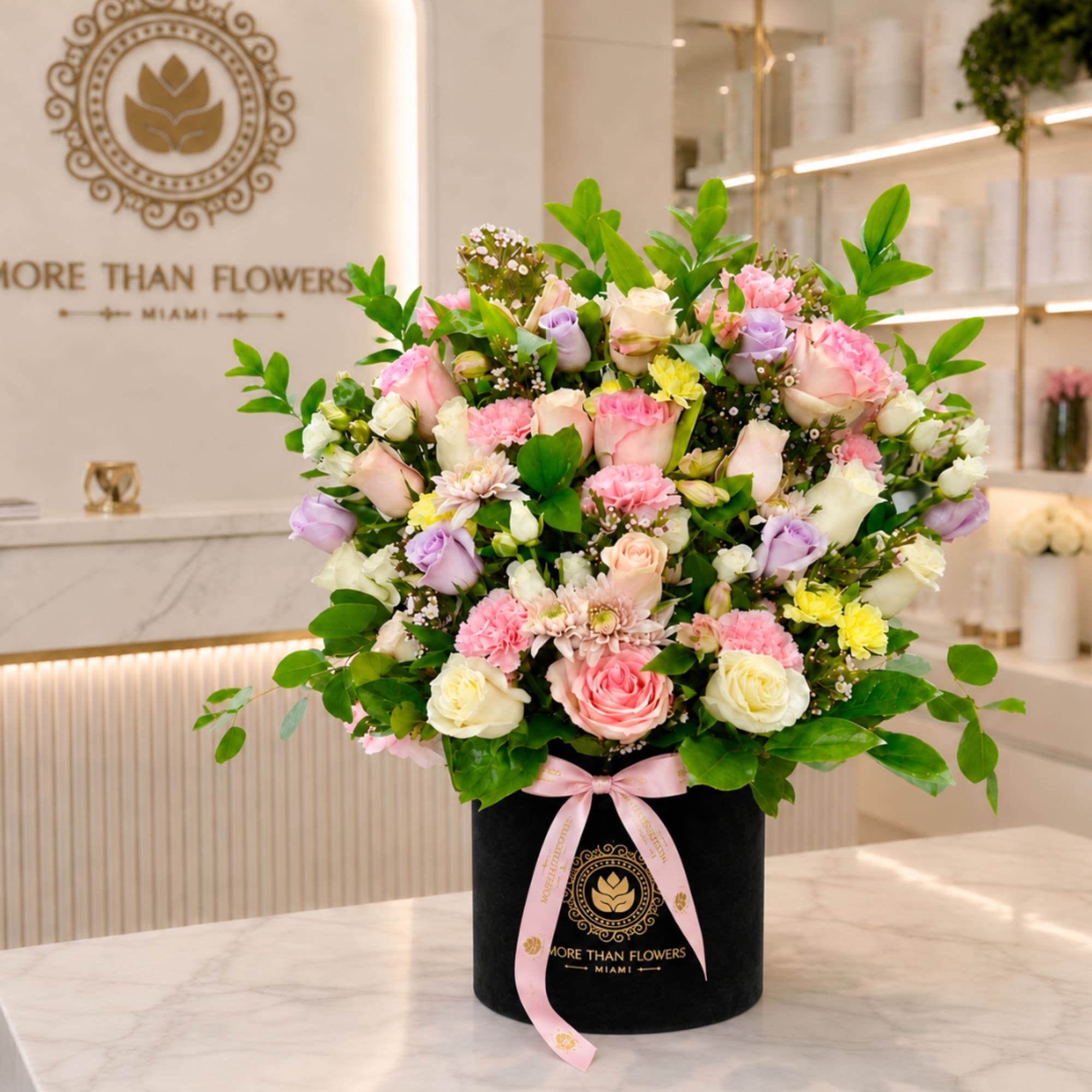 Mixed pastel roses and carnations in a black hatbox with a pink ribbon