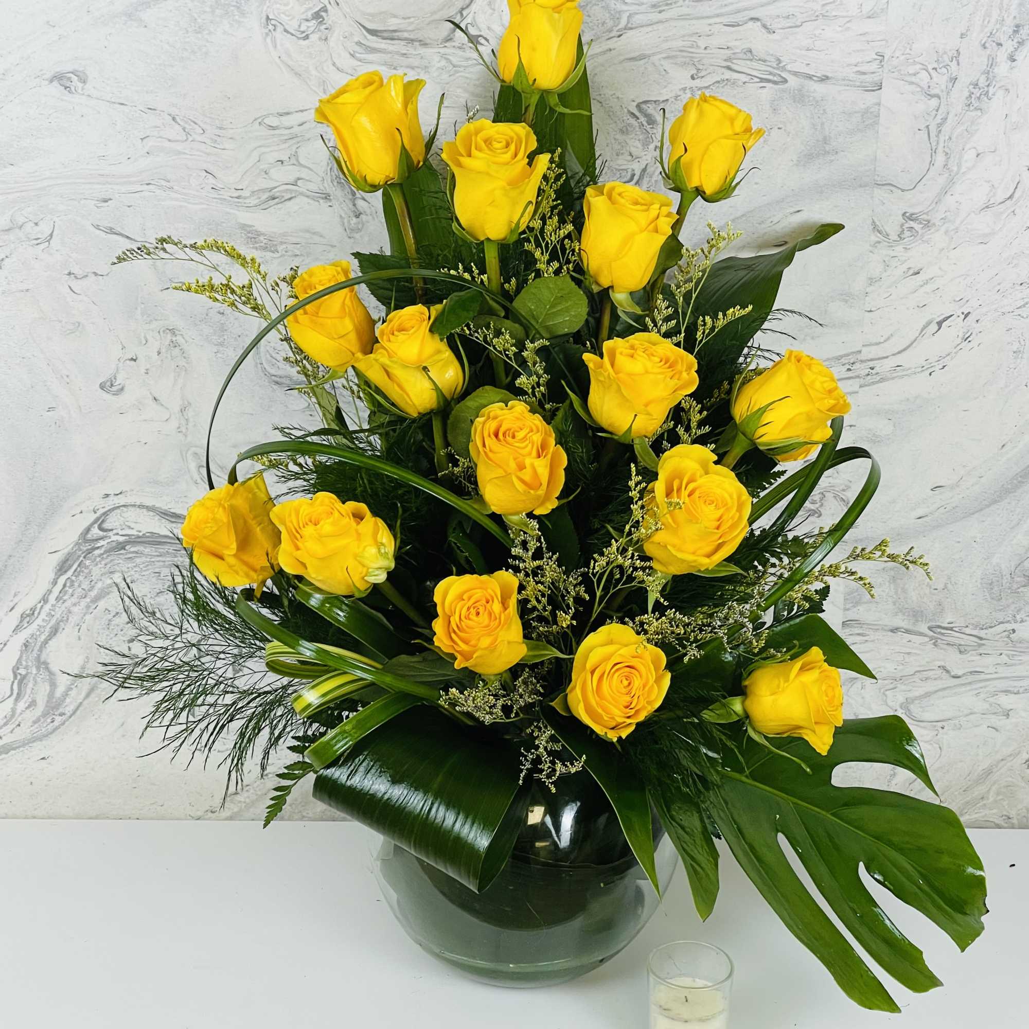 Yellow roses arranged in a glass vase with dark green foliage.