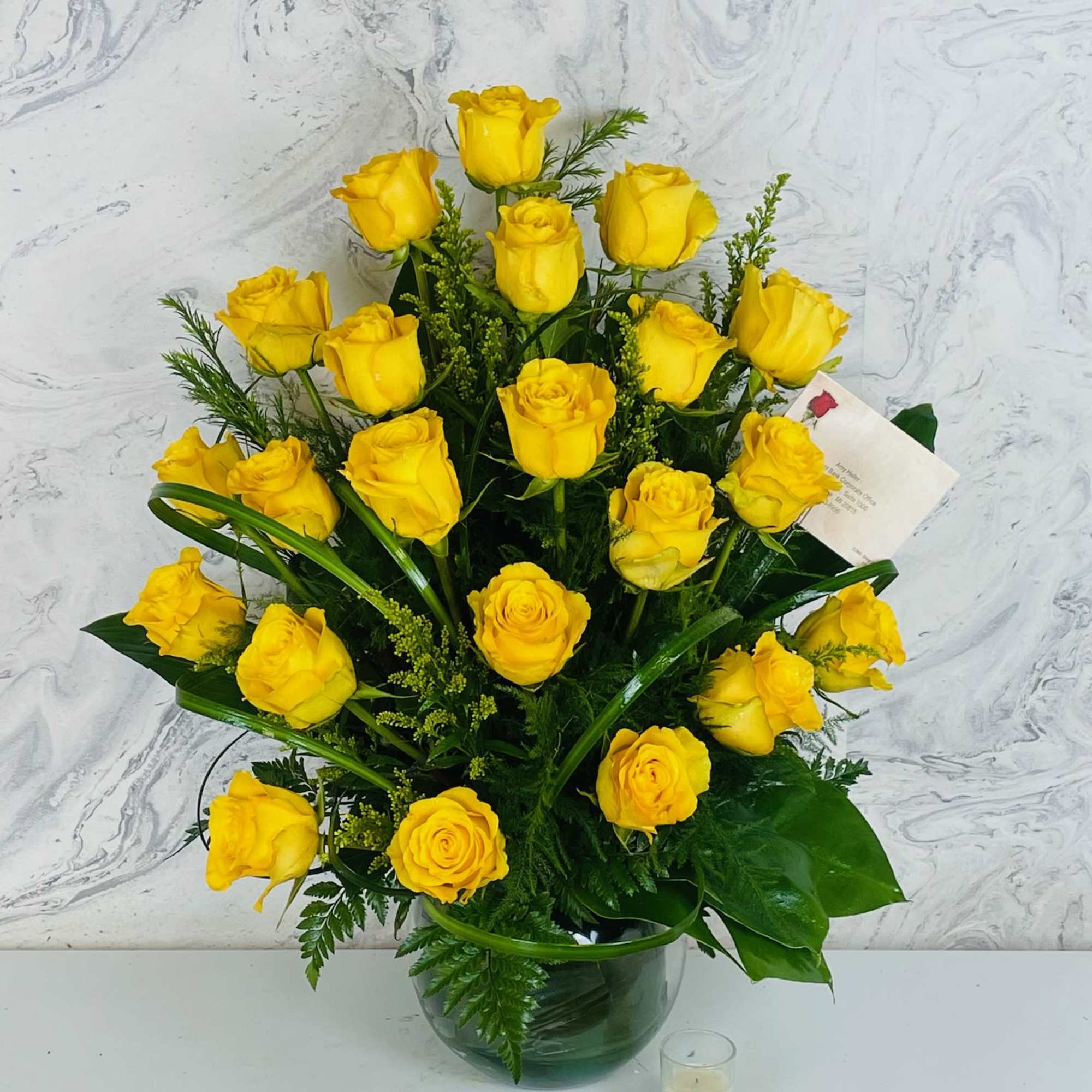 Yellow roses arranged in a glass vase with greenery
