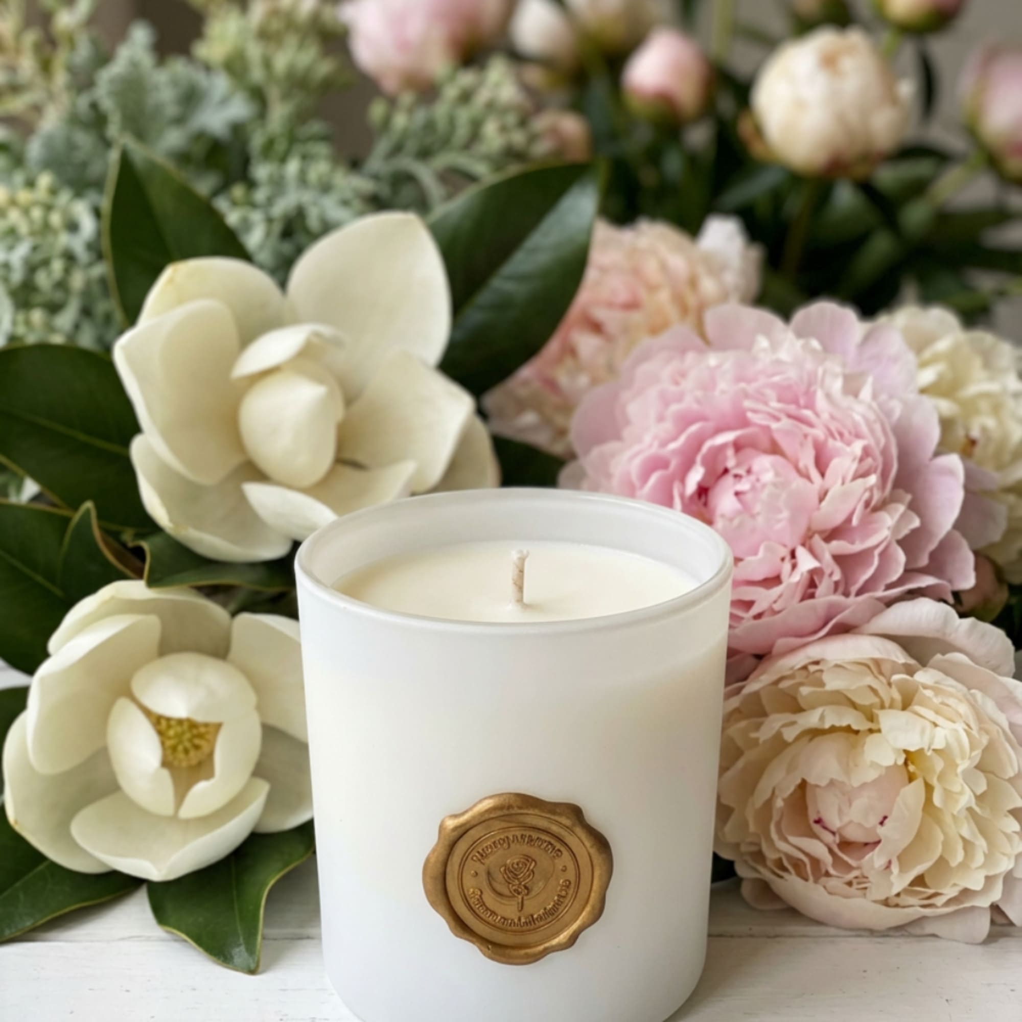 White candle in a glass jar surrounded by pink and cream flowers