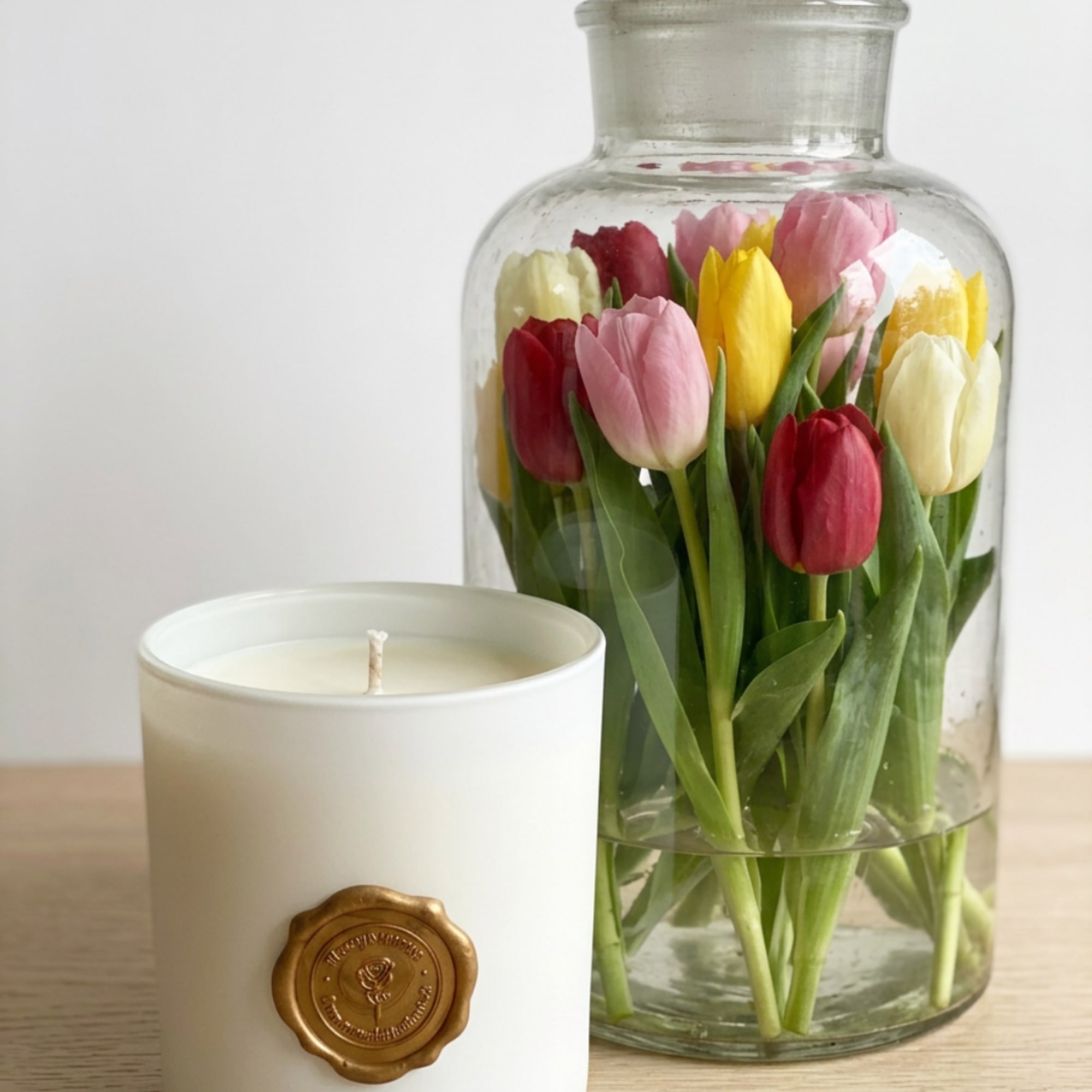 Tulips in a clear glass jar beside a white candle in a ceramic holder