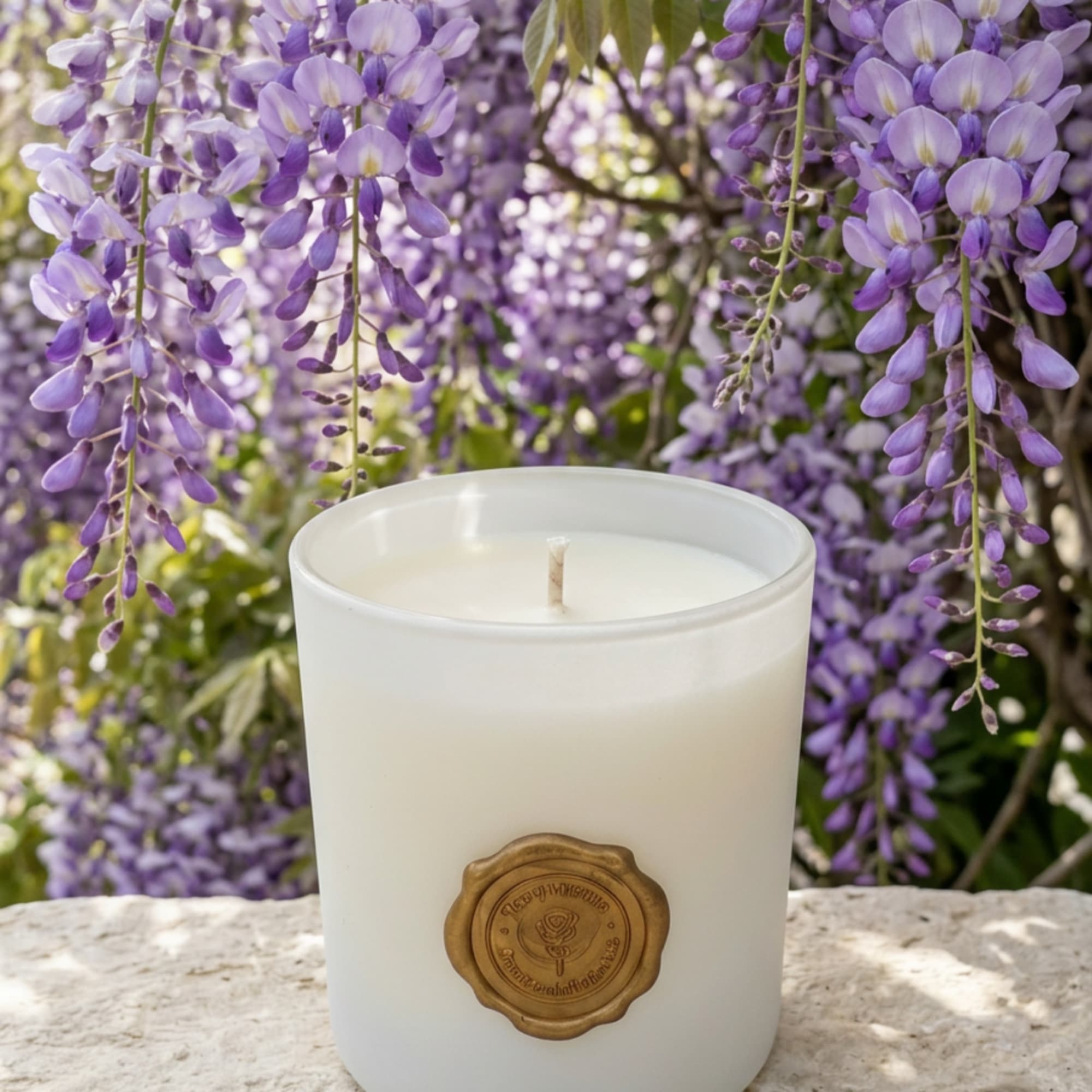 White candle in a glass jar with purple hanging flowers behind it