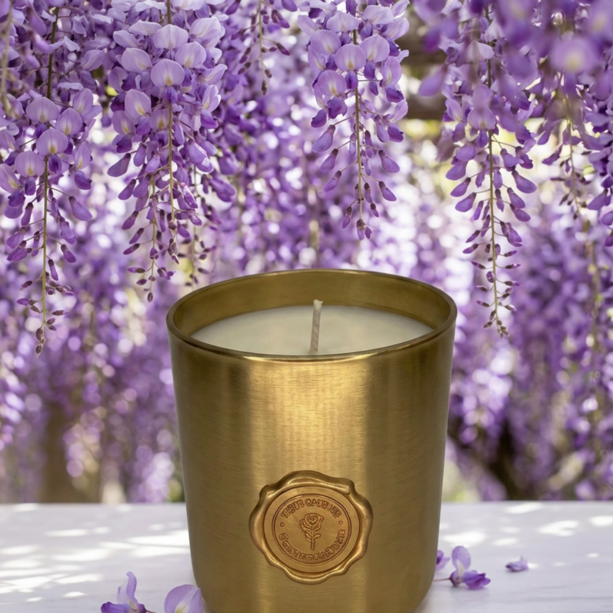 Gold candle in a metal cup with purple hanging blossoms behind it
