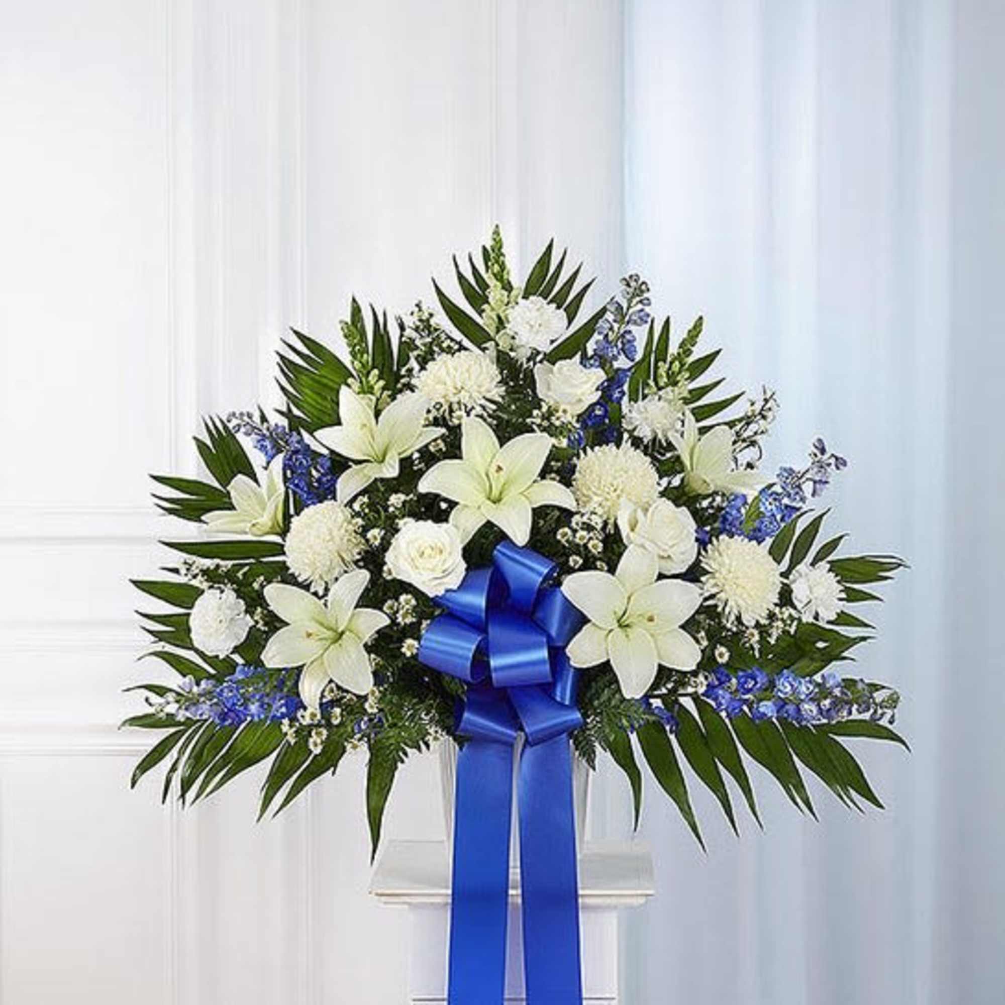 White lilies and blue flowers arranged with a large blue ribbon