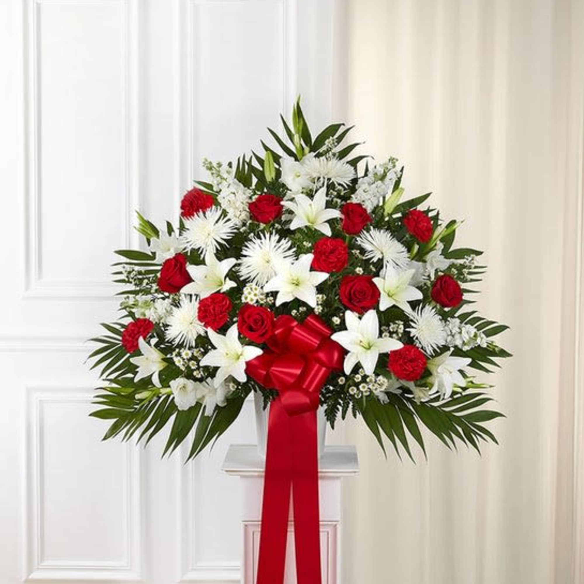 Standing floral spray of red roses and white lilies with a red ribbon