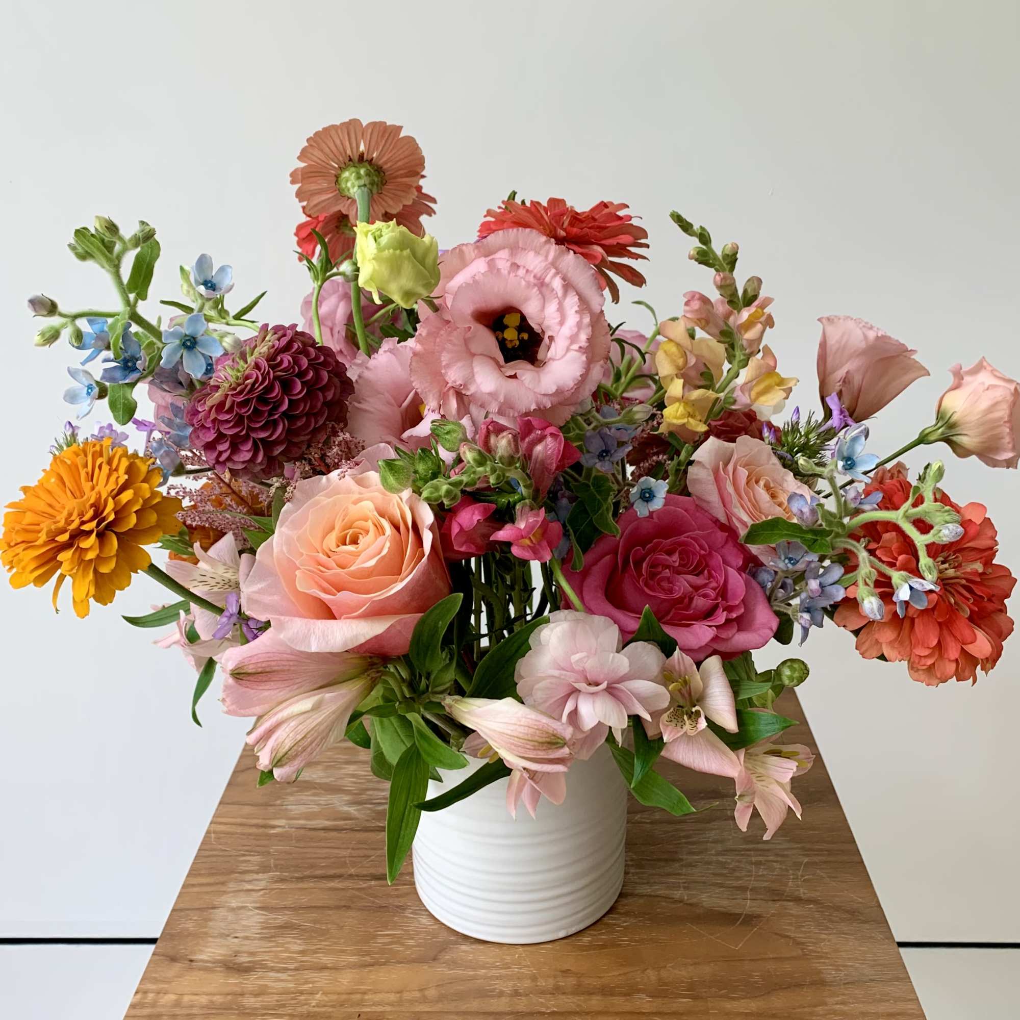 Mixed bouquet of pink, peach, orange, and blue flowers in a white vase