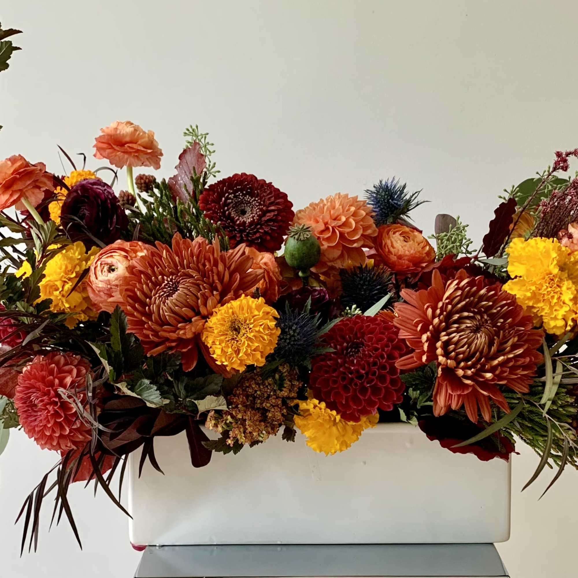 Autumn floral arrangement in a white rectangular container with orange, red, and yellow blooms