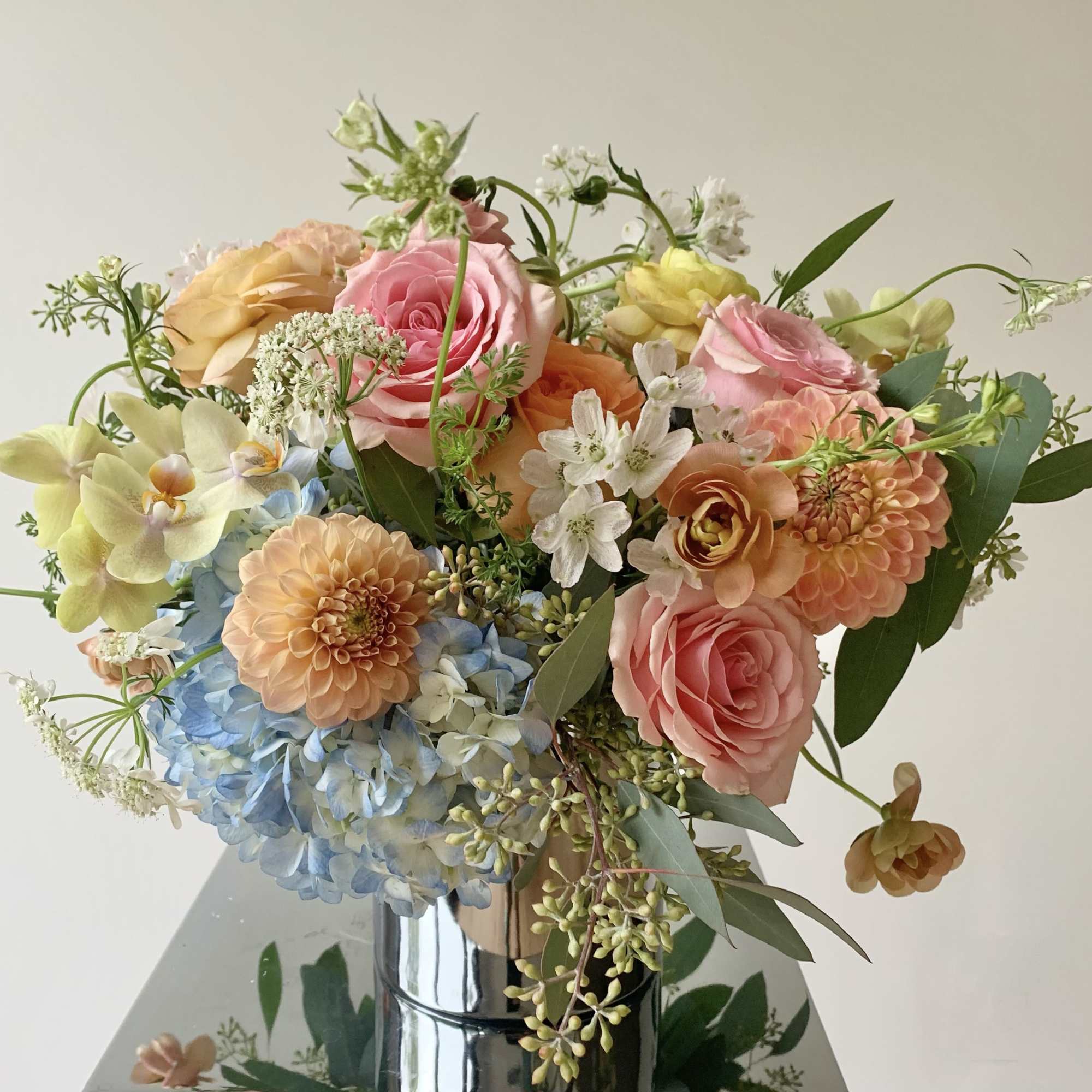 Bouquet of pastel roses, hydrangeas, and orchids in a reflective vase