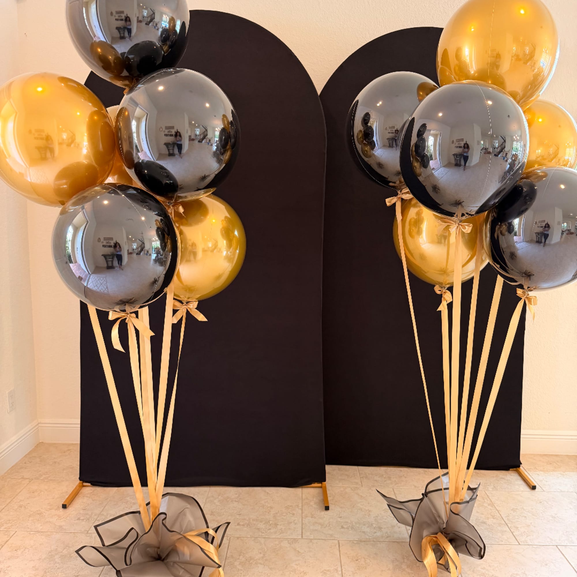 Gold and black balloon bouquets with ribbon tails in front of black backdrops