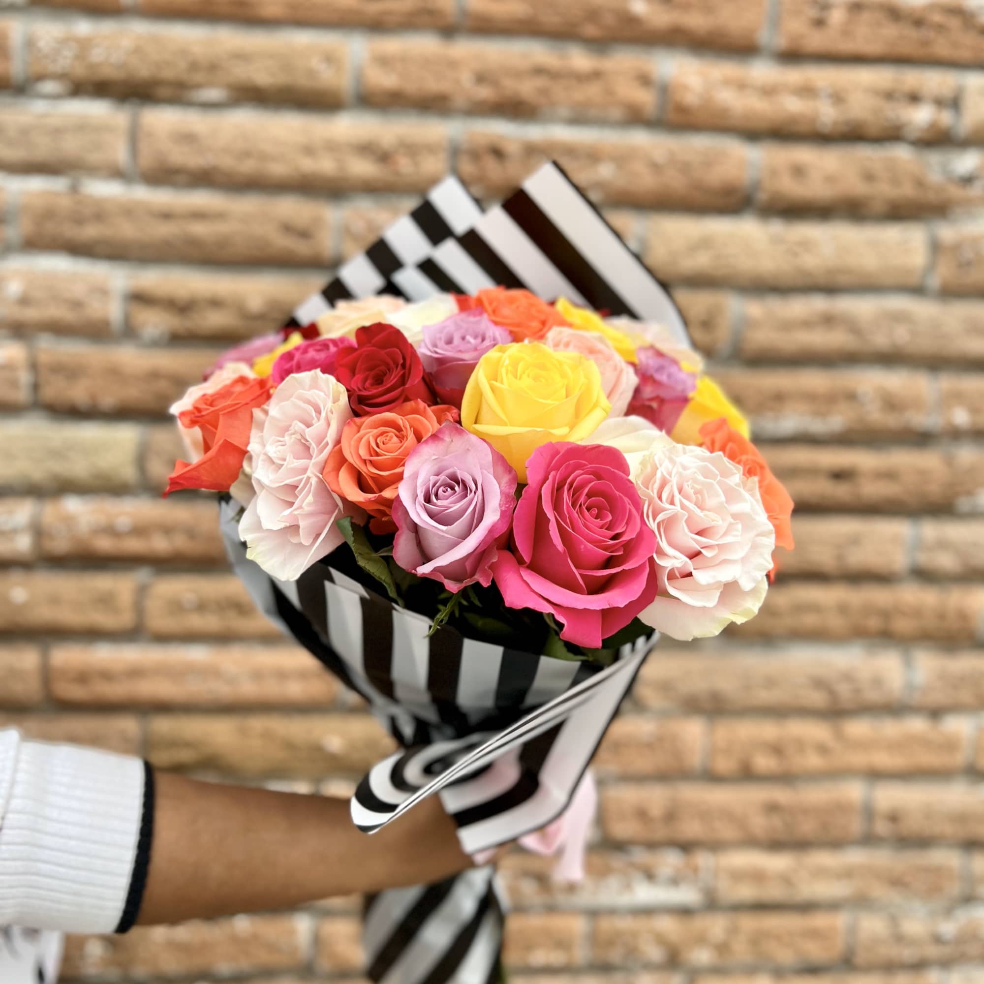 Handheld bouquet of multicolored roses wrapped in black-and-white striped paper