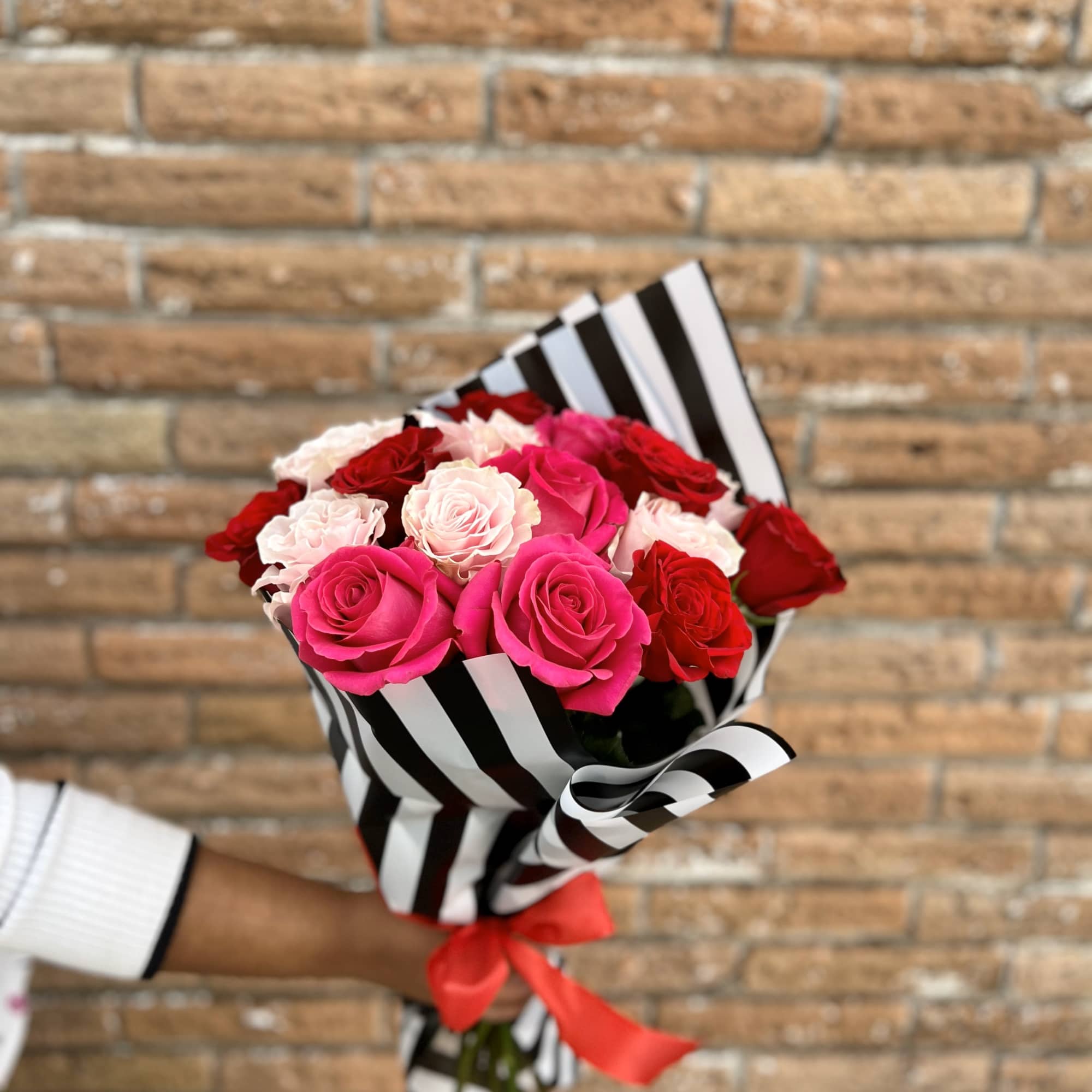 Handheld bouquet of pink, red, and white roses wrapped in black-and-white striped paper