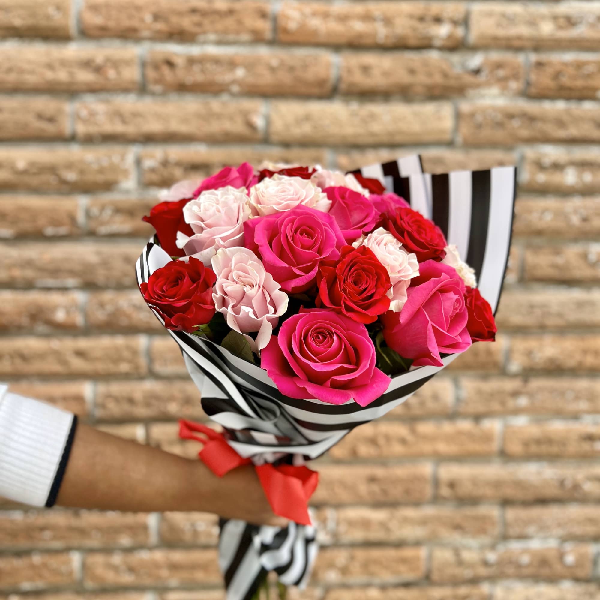Bouquet of pink, red, and pale roses wrapped in black-and-white striped paper