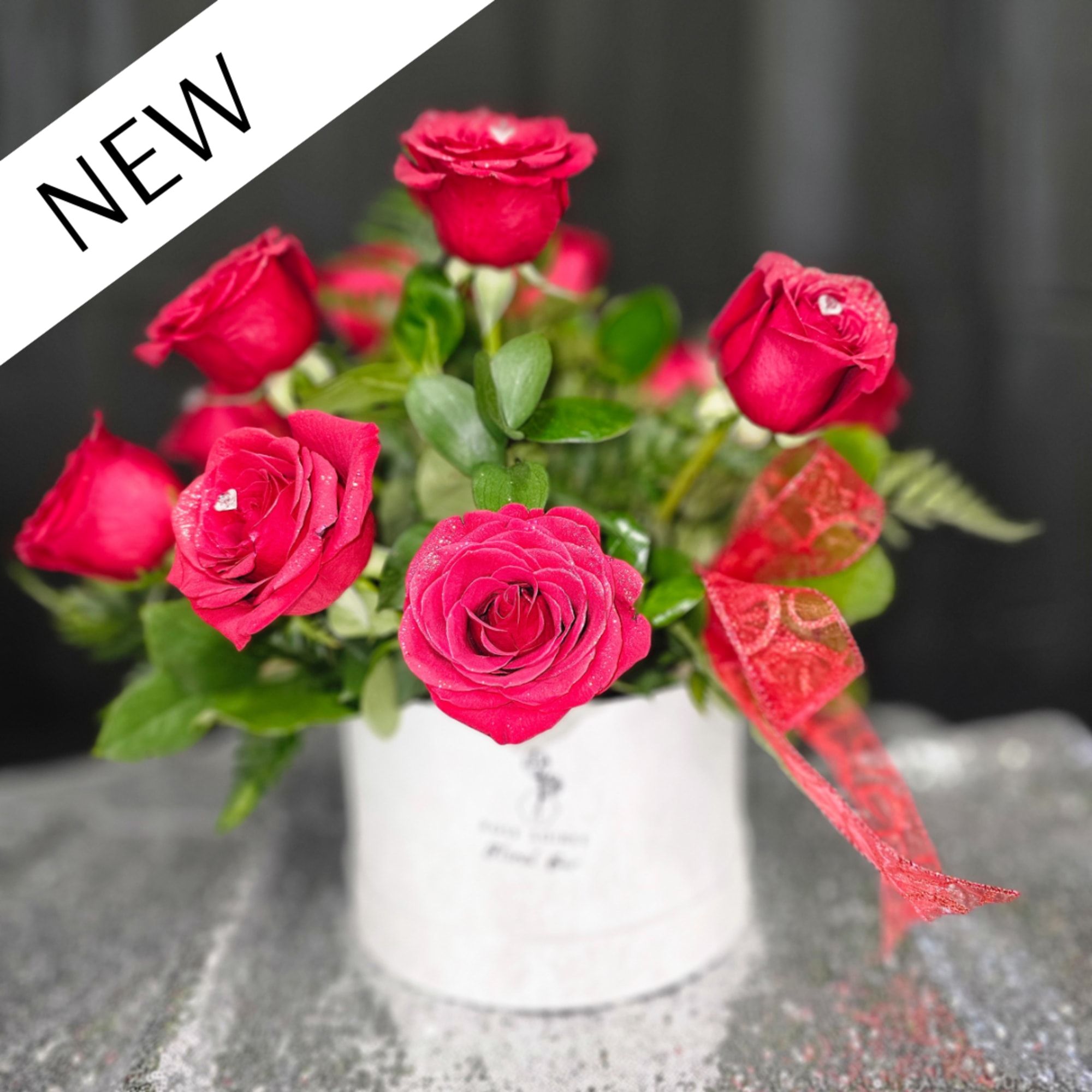 Hot pink roses in a white hatbox-style container with a red ribbon bow against a dark background