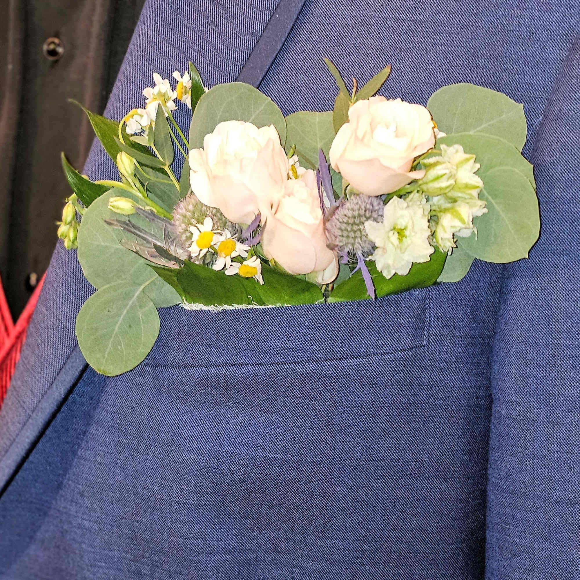 Boutonniere with pale roses and small white flowers on a blue suit jacket